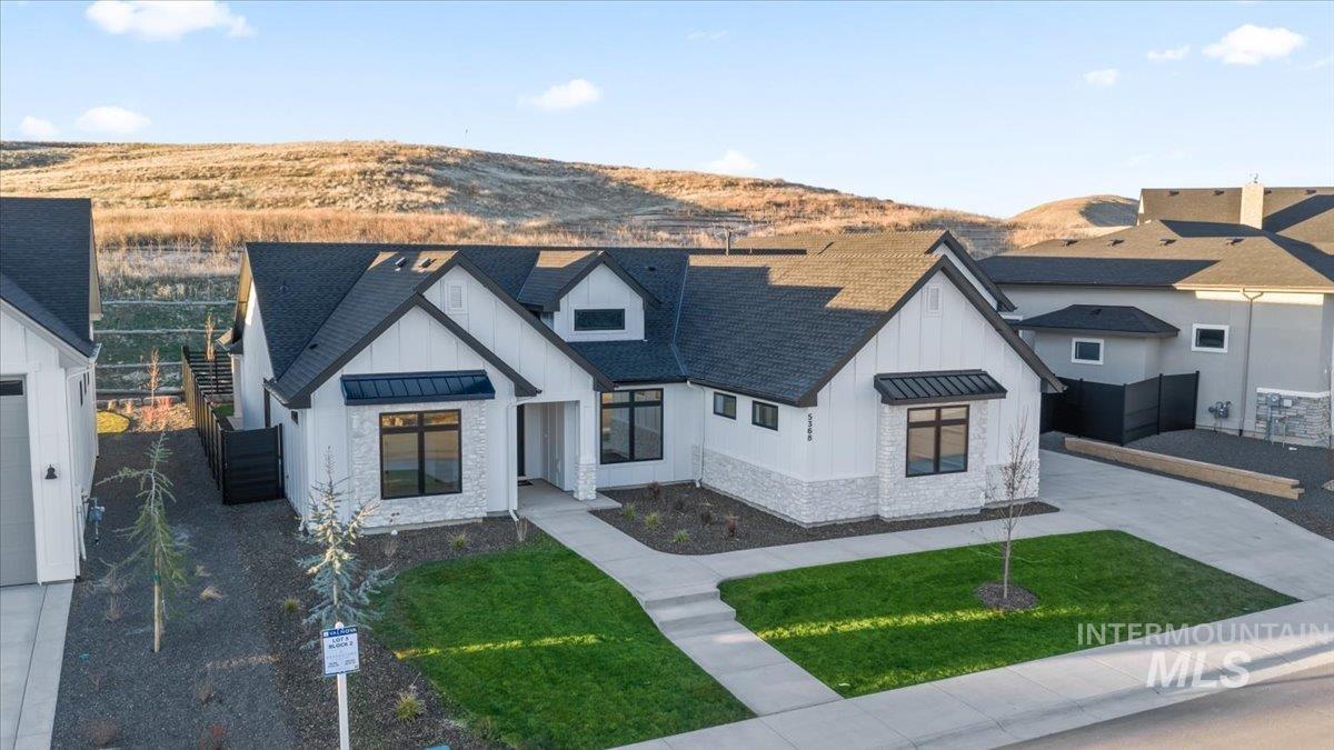 Modern farmhouse style home with a standing seam roof, board and batten siding, a metal roof, a shingled roof, and stone siding