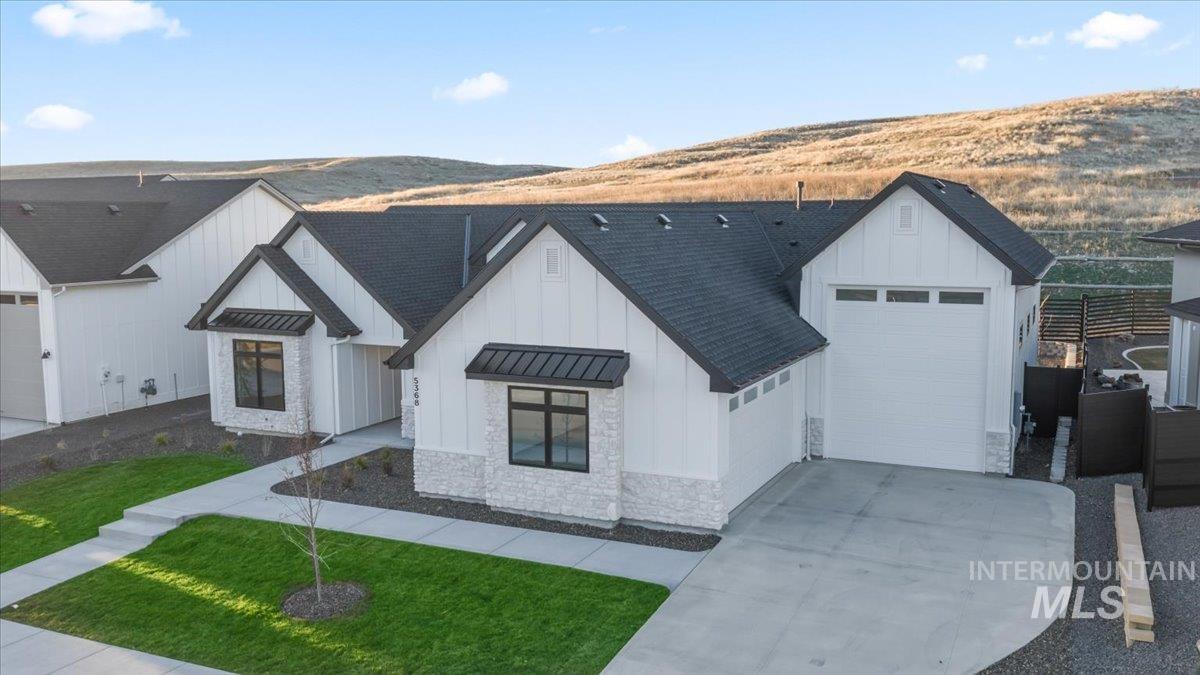 Modern inspired farmhouse with board and batten siding, a standing seam roof, a shingled roof, a metal roof, and driveway