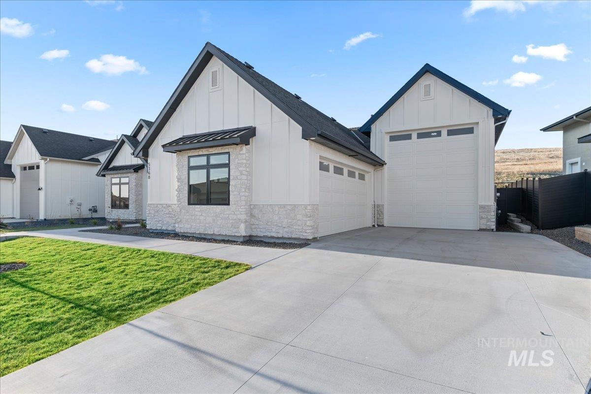 Modern inspired farmhouse with a standing seam roof, board and batten siding, stone siding, concrete driveway, and a metal roof