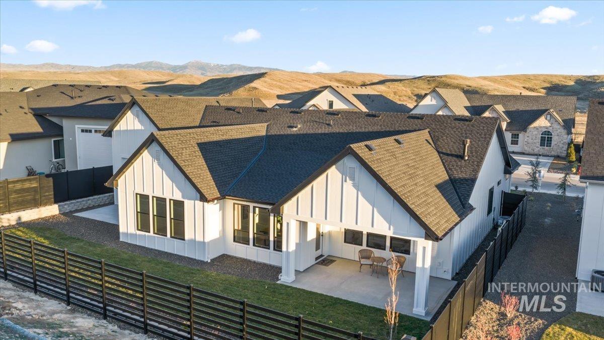 Rear view of house with board and batten siding, a patio area, a fenced backyard, and a shingled roof
