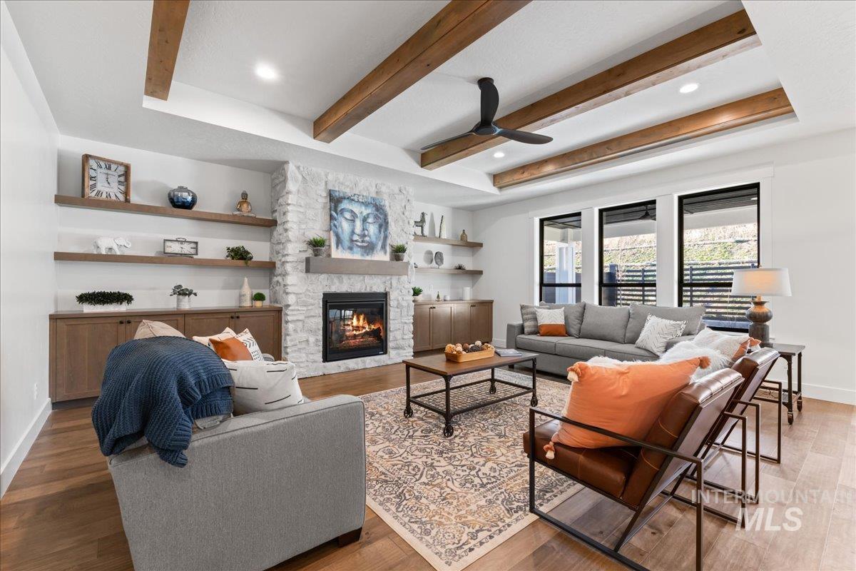 Living area with wood finished floors, a stone fireplace, a ceiling fan, beamed ceiling, and recessed lighting