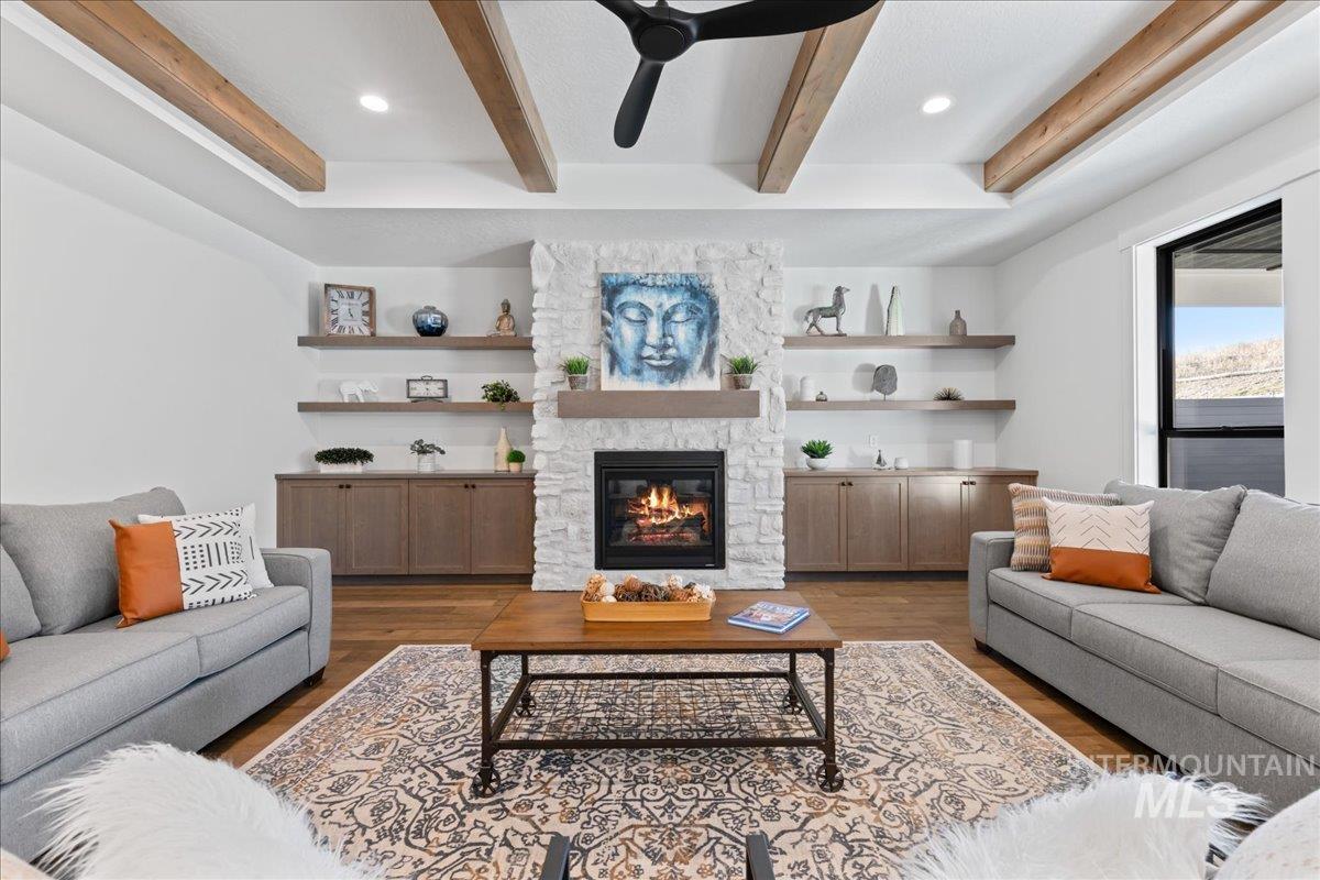 Living area featuring beam ceiling, wood finished floors, a stone fireplace, a ceiling fan, and recessed lighting