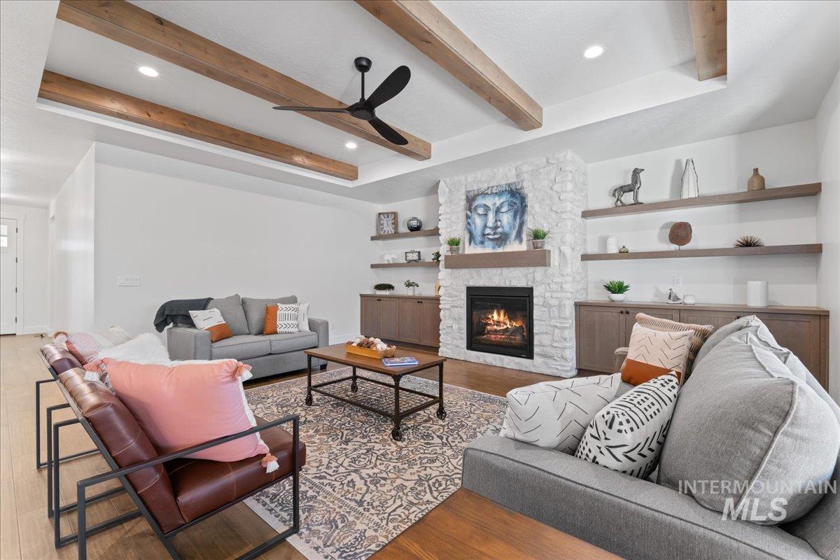 Living area featuring beam ceiling, a stone fireplace, wood finished floors, recessed lighting, and a ceiling fan