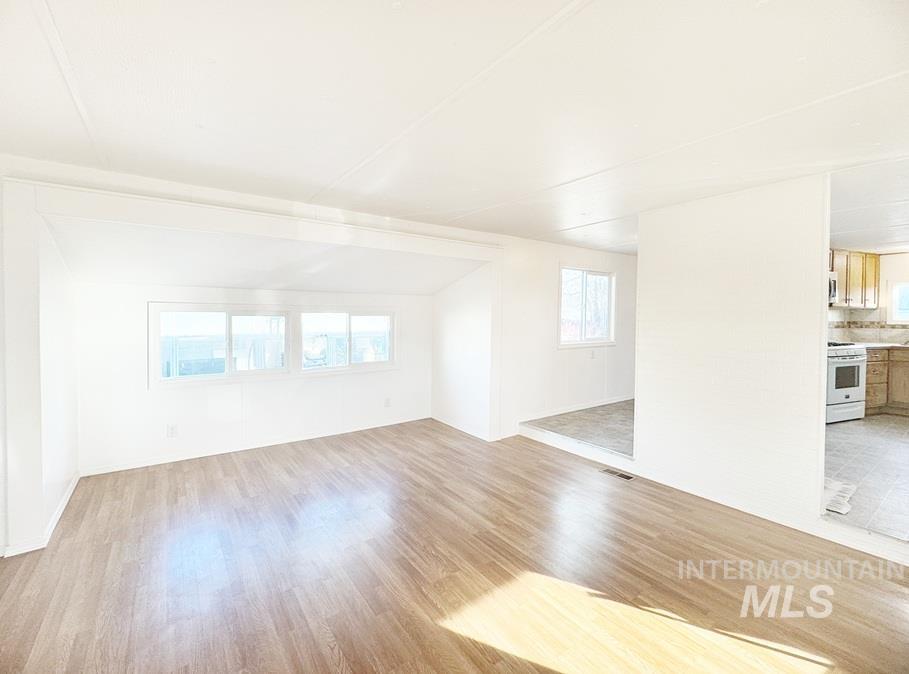 Unfurnished living room with light wood-style flooring, plenty of natural light, and vaulted ceiling