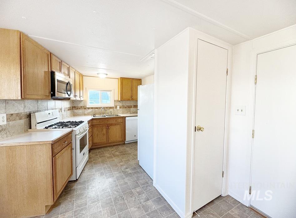 Kitchen with white appliances, light countertops, backsplash, brown cabinets, and light flooring
