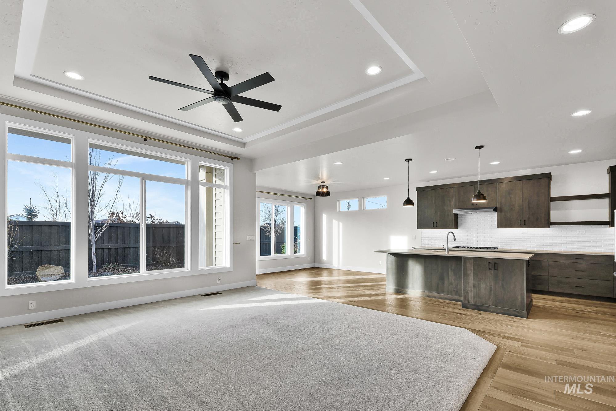 Living room featuring a ceiling fan, a tray ceiling, light wood finished floors, and recessed lighting