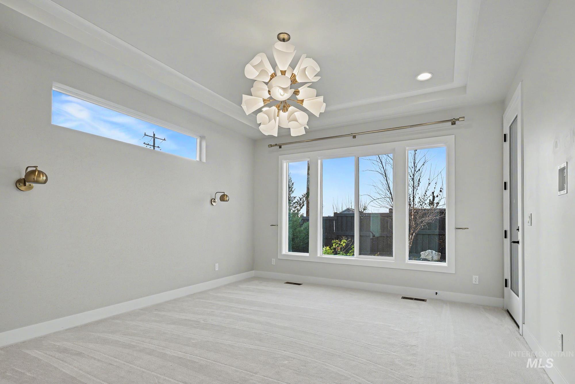 Empty room with a chandelier, light colored carpet, and a tray ceiling