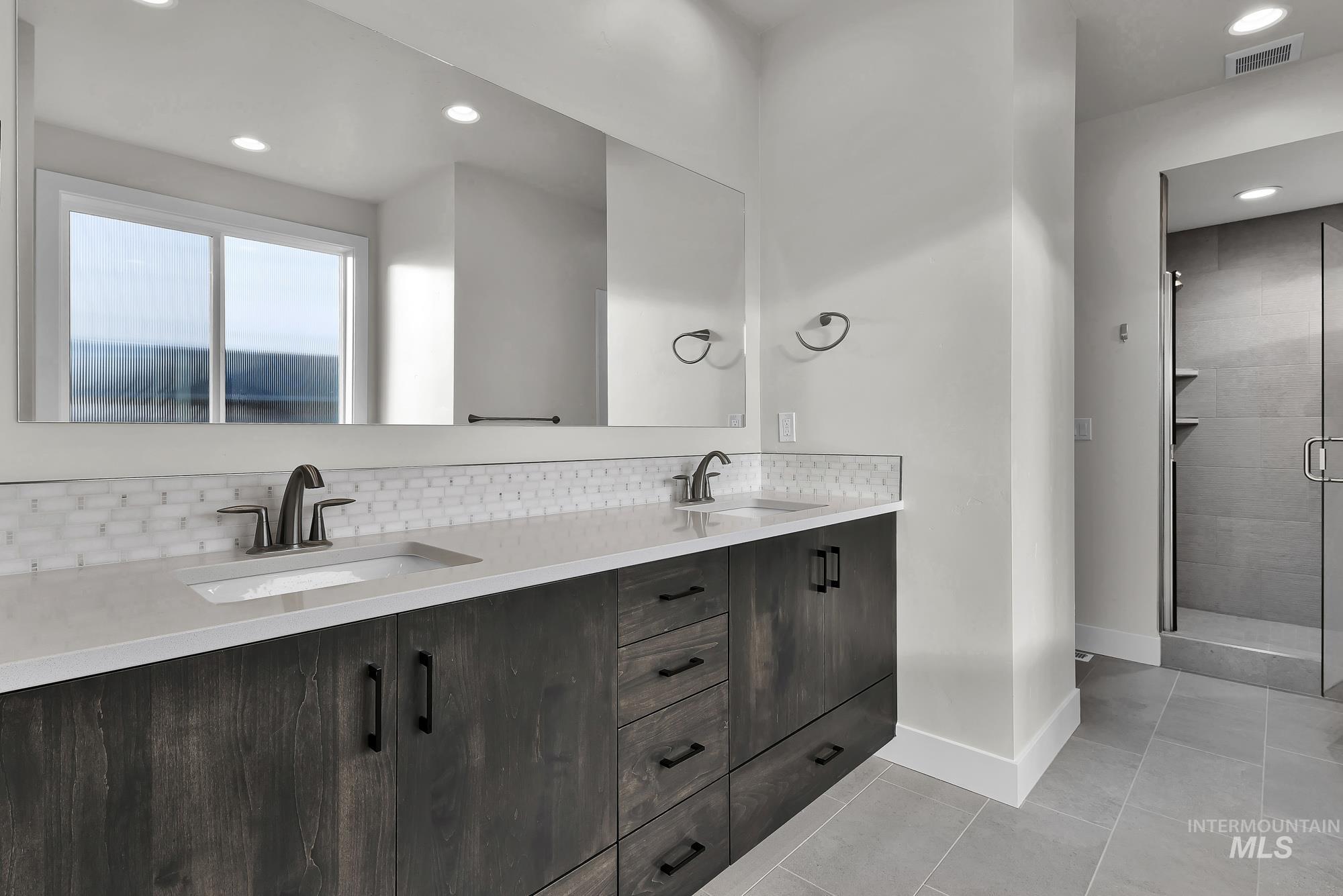 Full bath featuring double vanity, recessed lighting, light tile patterned floors, decorative backsplash, and a shower stall
