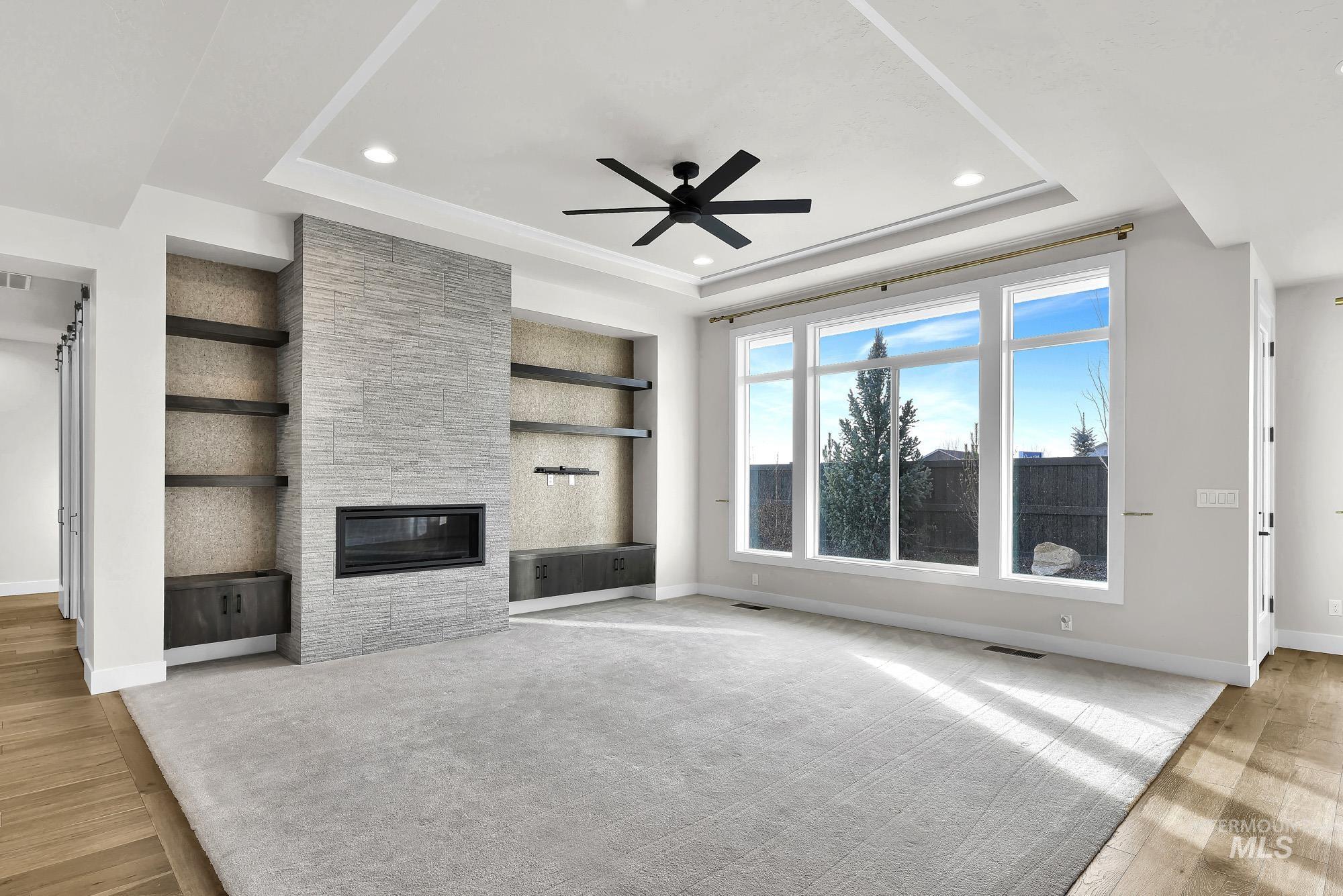 Unfurnished living room featuring built in features, light wood-style flooring, a stone fireplace, ceiling fan, and recessed lighting