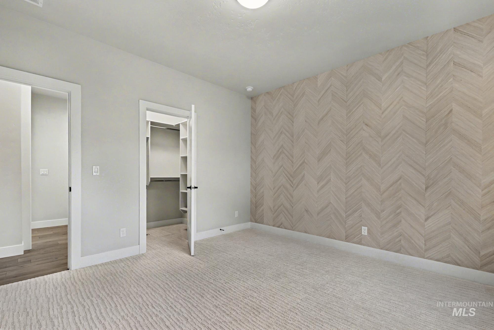 Unfurnished bedroom with a spacious closet, carpet flooring, and an accent wall