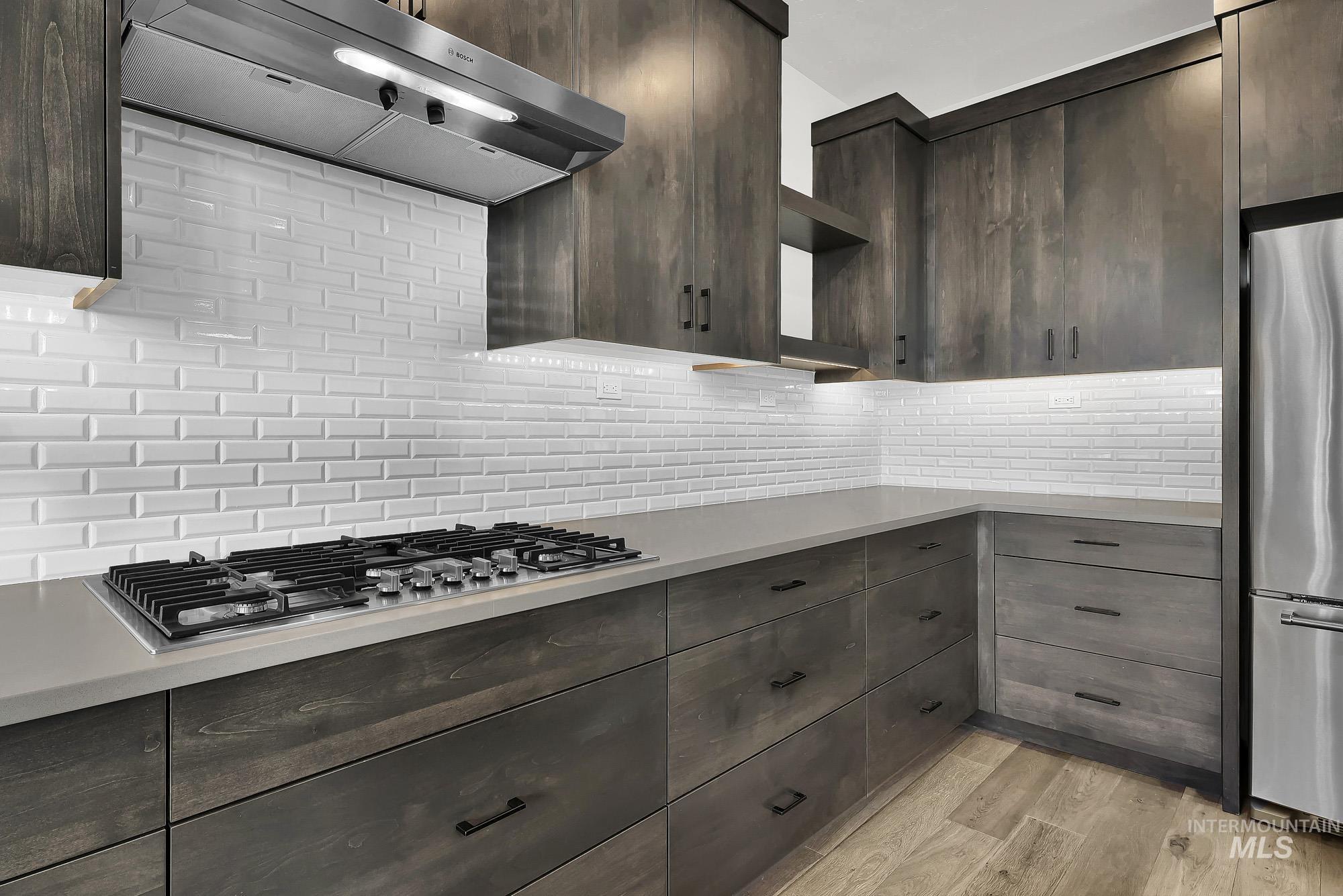 Kitchen featuring under cabinet range hood, open shelves, stainless steel appliances, and dark brown cabinetry