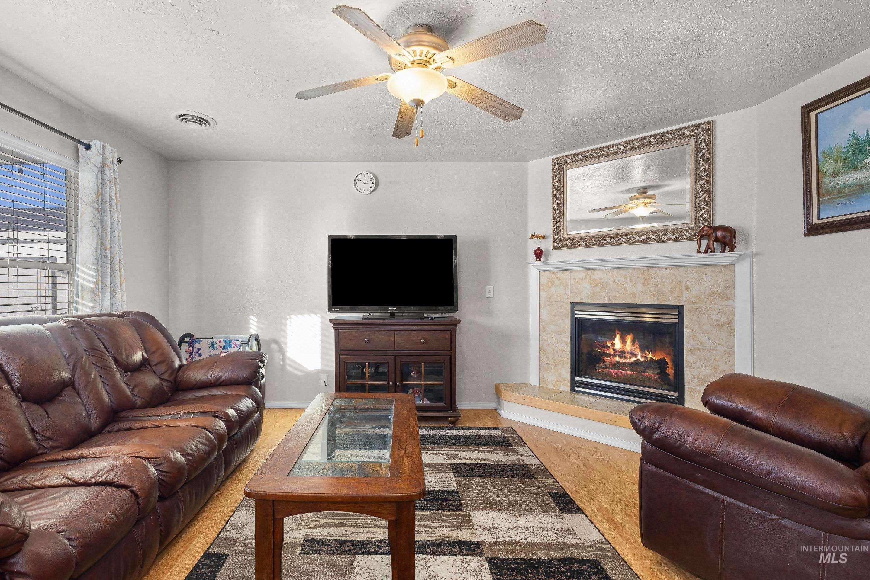 Living area featuring a ceiling fan, a tiled fireplace, wood finished floors, and a textured ceiling