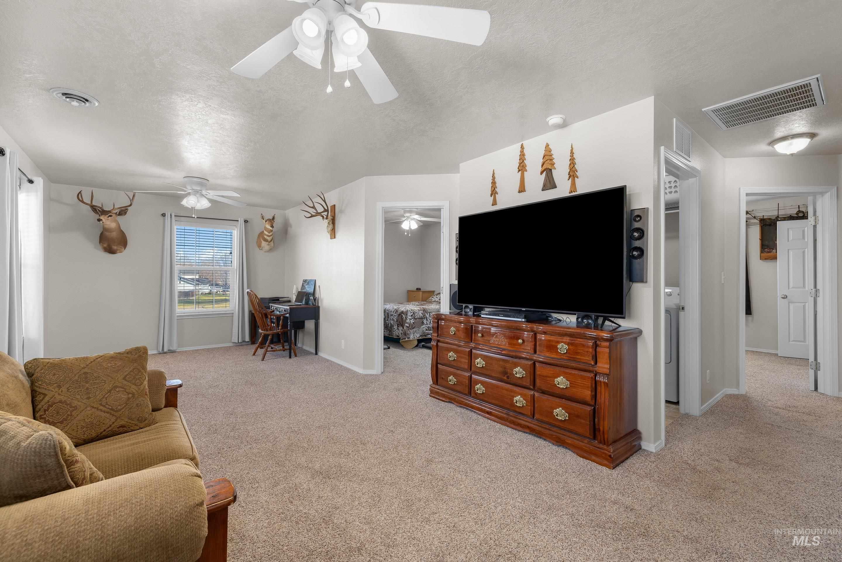 Living area with light carpet, a textured ceiling, and a desk