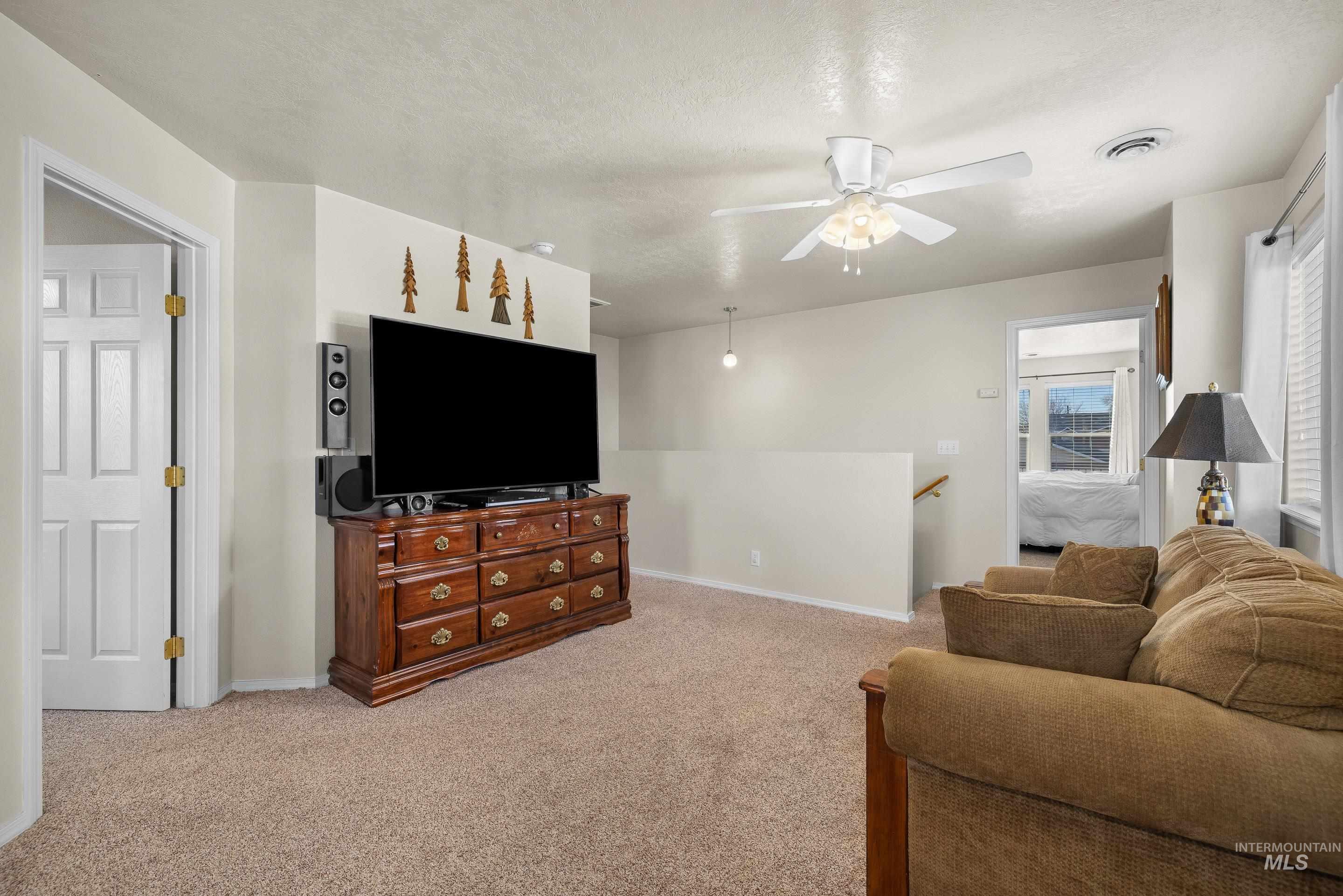 Living room with light colored carpet, a ceiling fan, and a textured ceiling