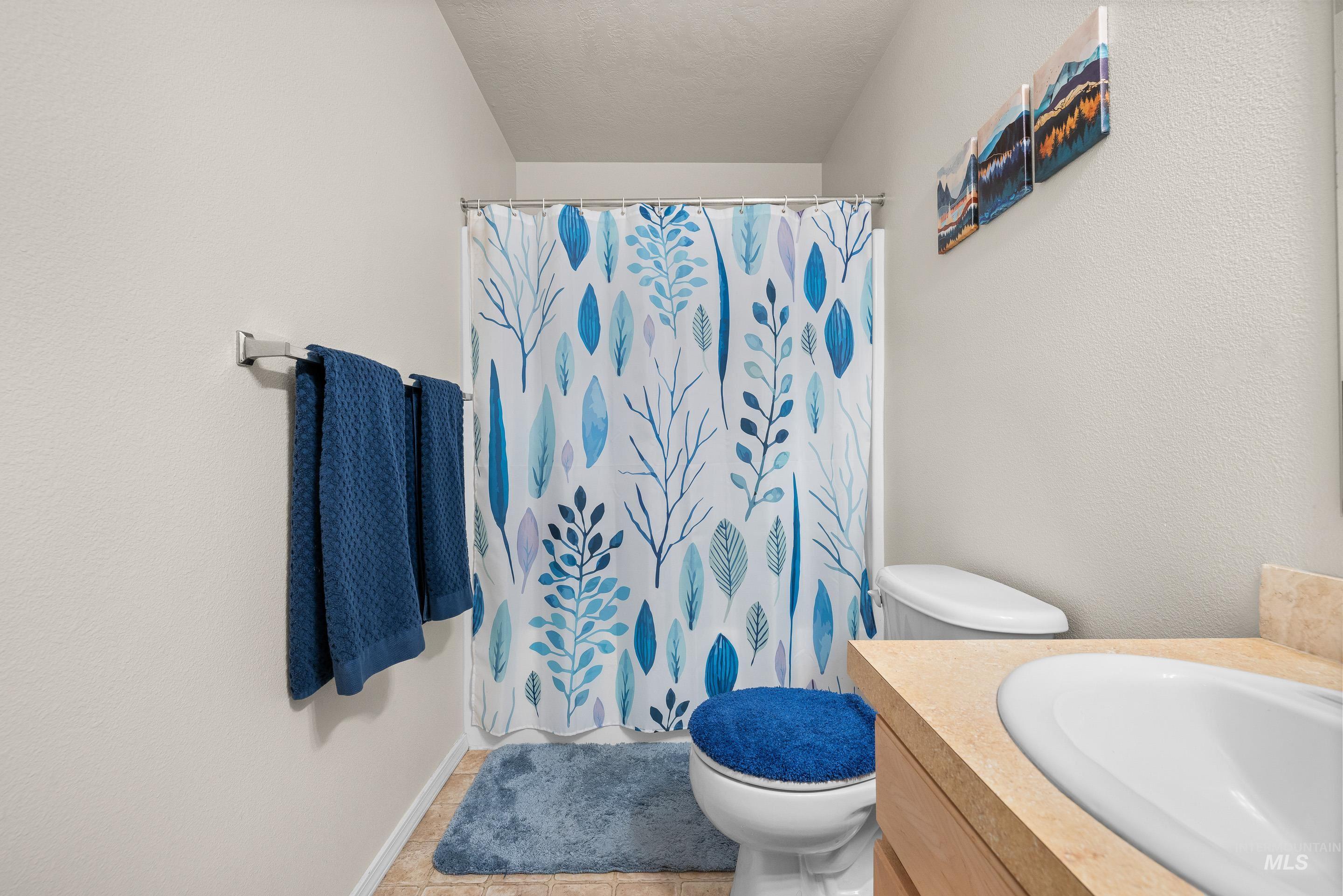 Full bath with a shower with shower curtain, vanity, tile patterned floors, a textured wall, and a textured ceiling