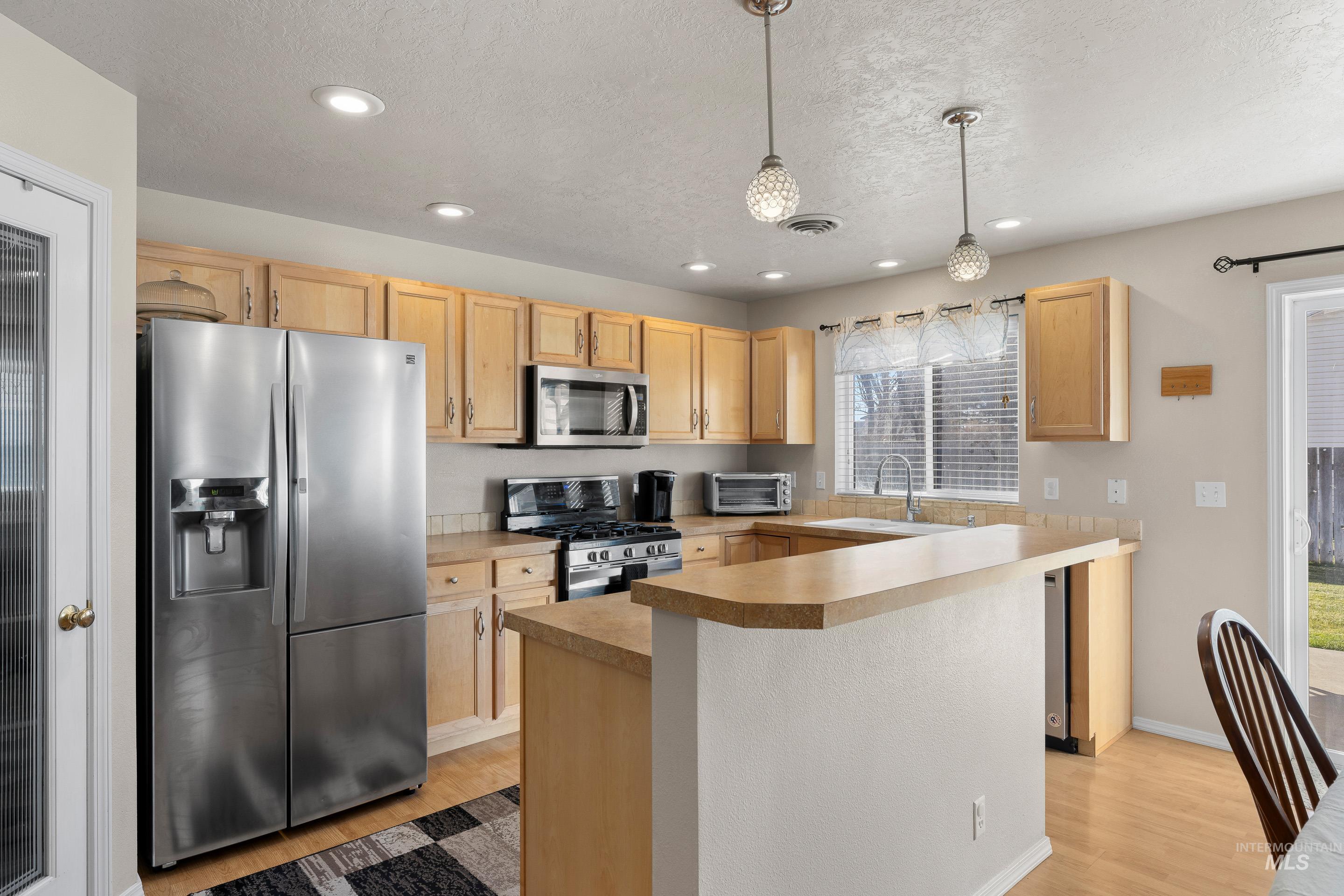 Kitchen with appliances with stainless steel finishes, light brown cabinets, hanging light fixtures, light wood-style flooring, and recessed lighting