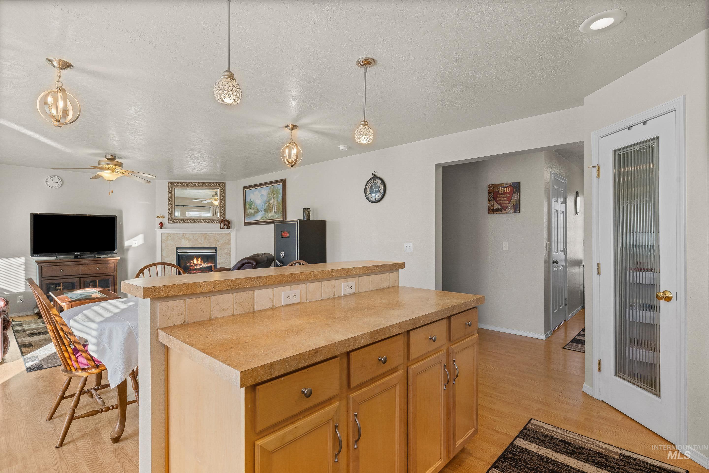 Kitchen with open floor plan, a warm lit fireplace, decorative light fixtures, a kitchen island, and light countertops