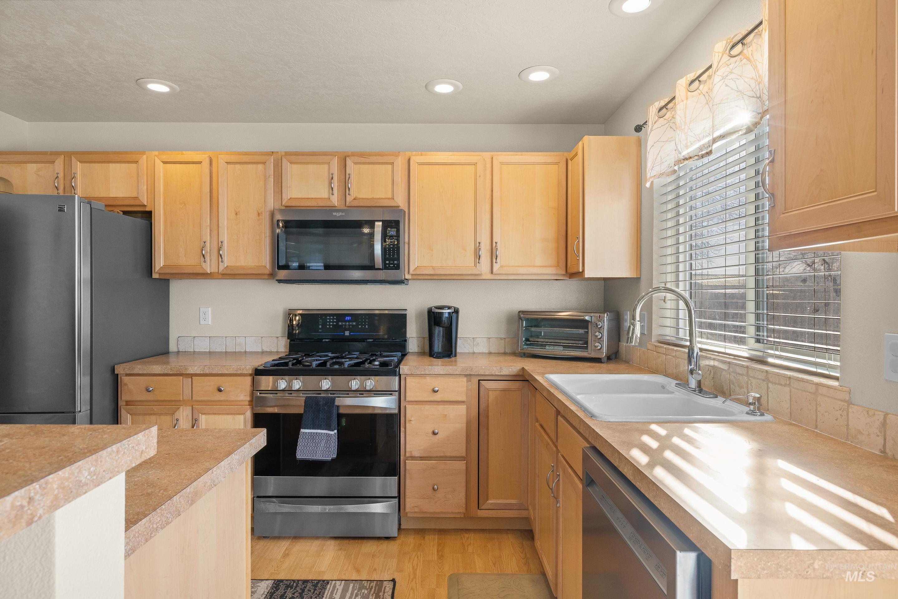 Kitchen with appliances with stainless steel finishes, light countertops, light wood-type flooring, light brown cabinets, and recessed lighting