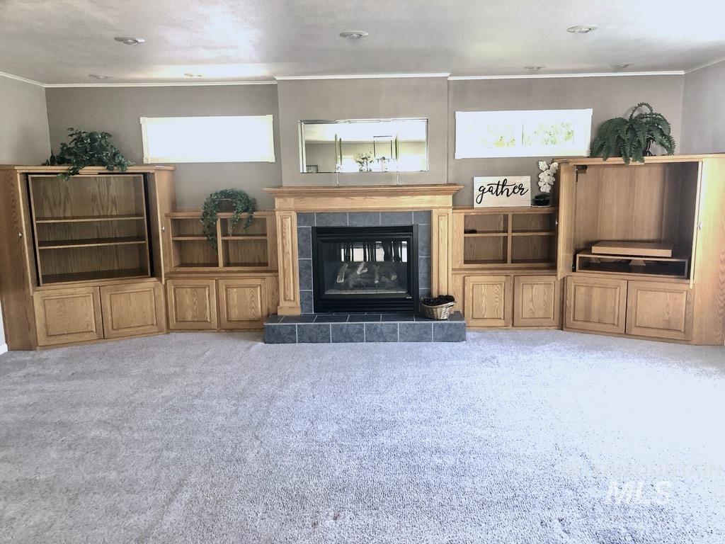 Living area featuring a tile fireplace, light carpet, and ornamental molding