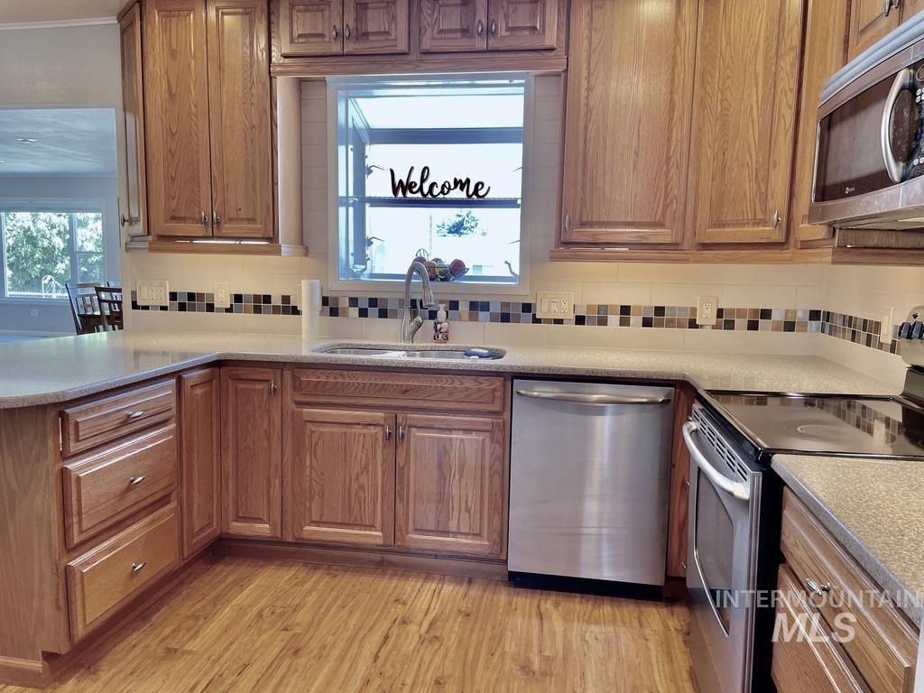 Kitchen with appliances with stainless steel finishes, brown cabinetry, backsplash, light wood finished floors, and light stone counters