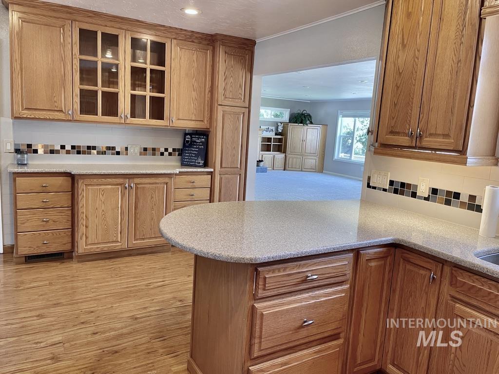 Kitchen featuring decorative backsplash, glass insert cabinets, brown cabinets, crown molding, and light stone countertops