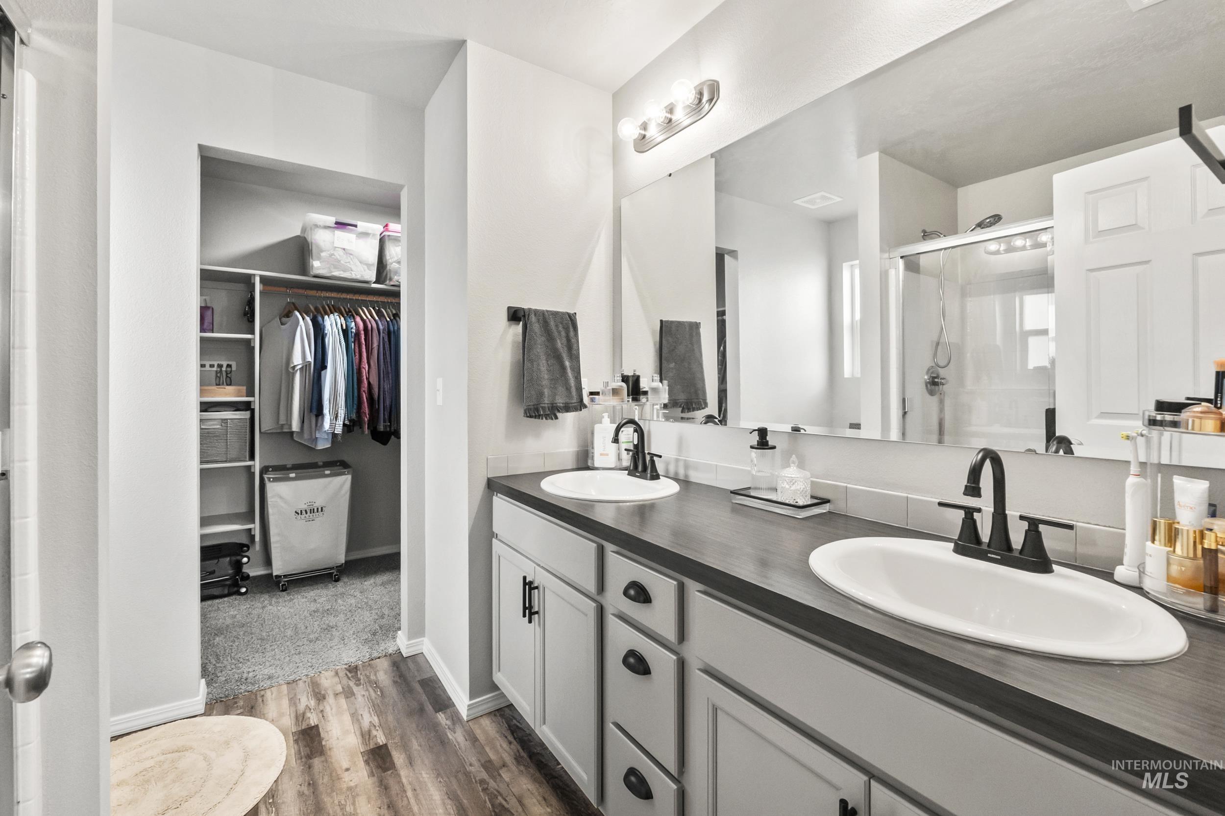 Full bathroom with a stall shower, double vanity, a walk in closet, and dark wood-style floors