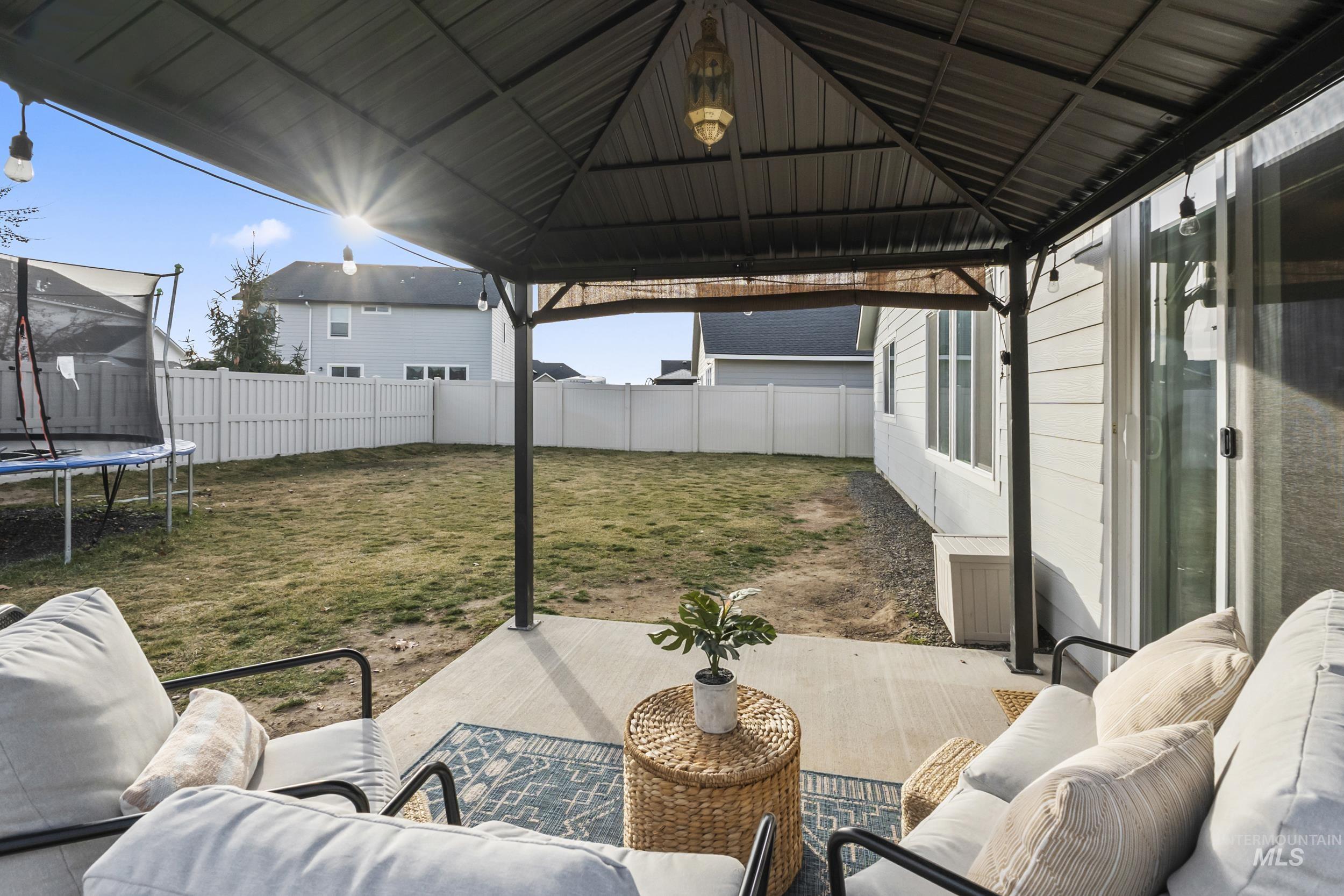 Fenced backyard featuring an outdoor hangout area, a trampoline, and a patio area