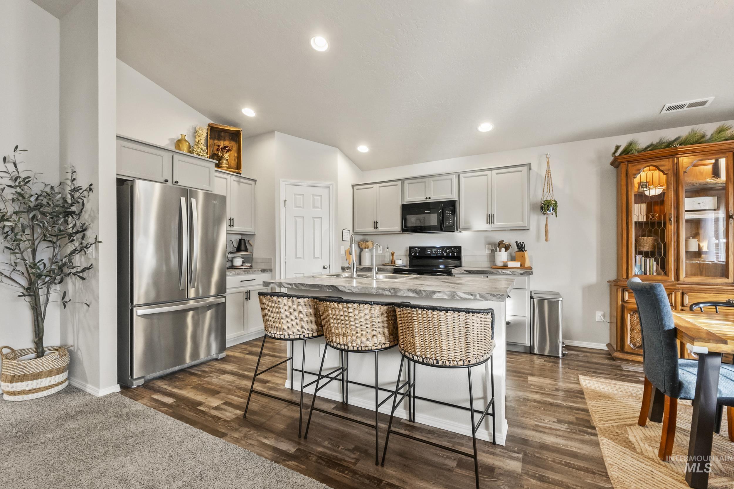Kitchen with black appliances, a breakfast bar area, a kitchen island with sink, light stone counters, and recessed lighting