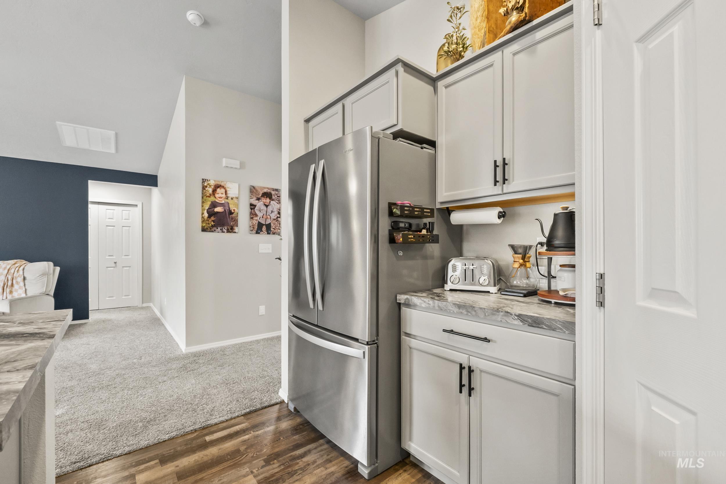 Kitchen with freestanding refrigerator, light stone countertops, dark wood finished floors, dark colored carpet, and open floor plan