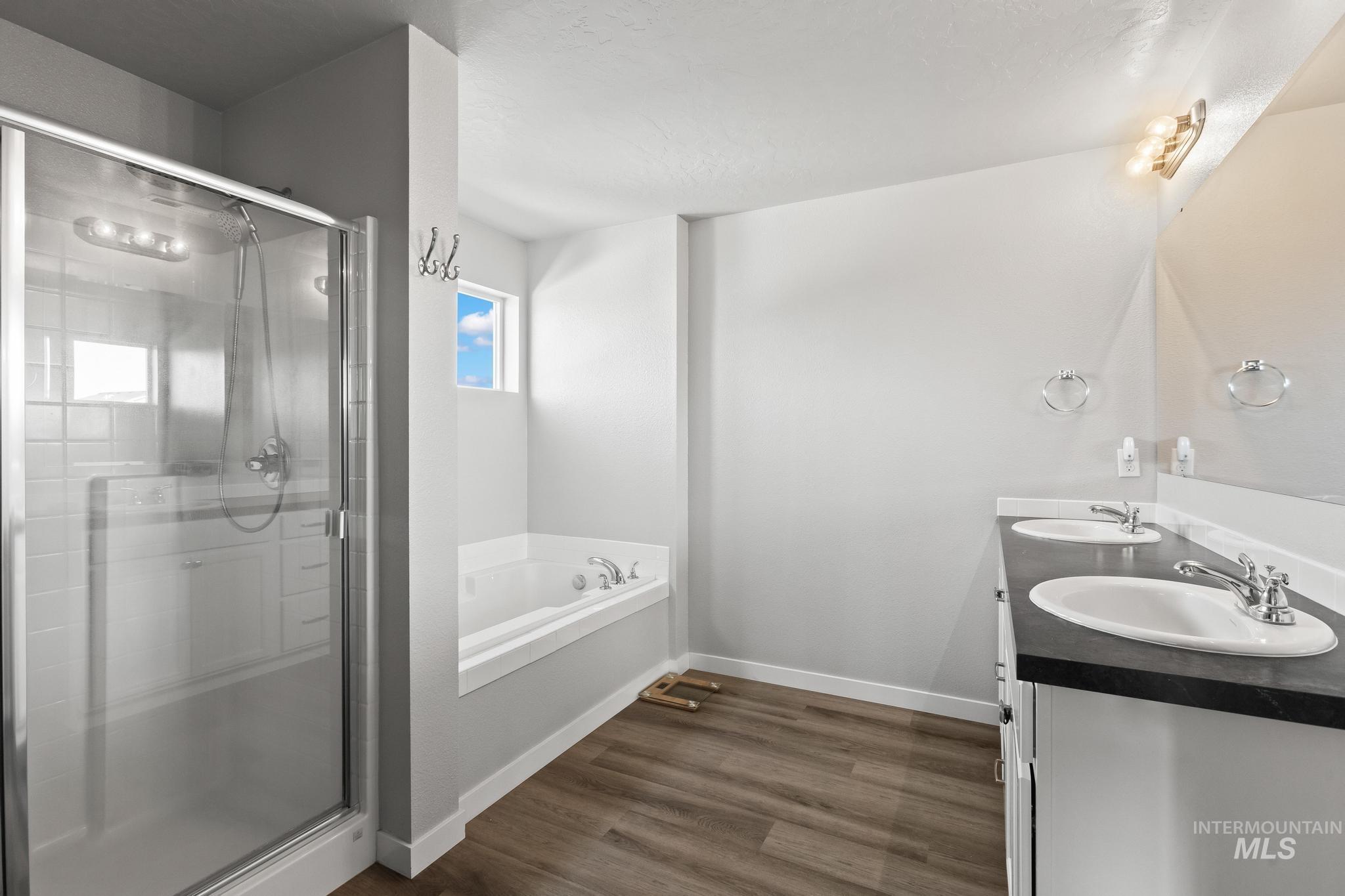Full bathroom with double vanity, a garden tub, dark wood-style flooring, and a stall shower