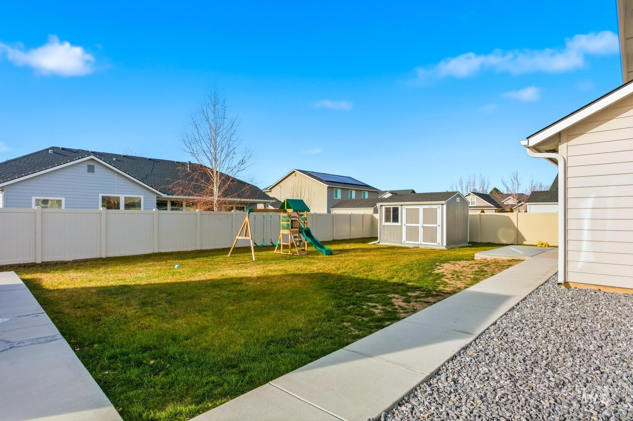 Fenced backyard with a playground, a storage shed, and a residential view