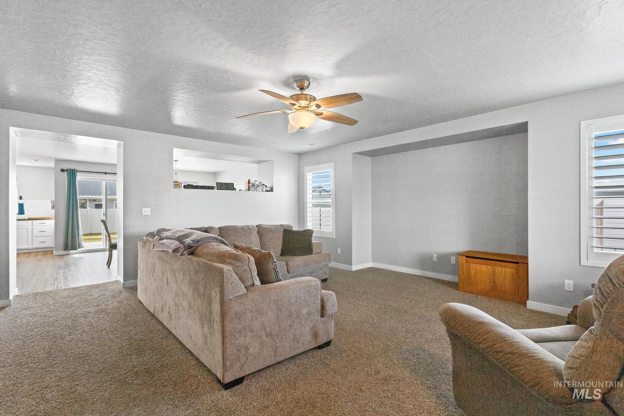 Living room featuring ceiling fan, a textured ceiling, and carpet flooring