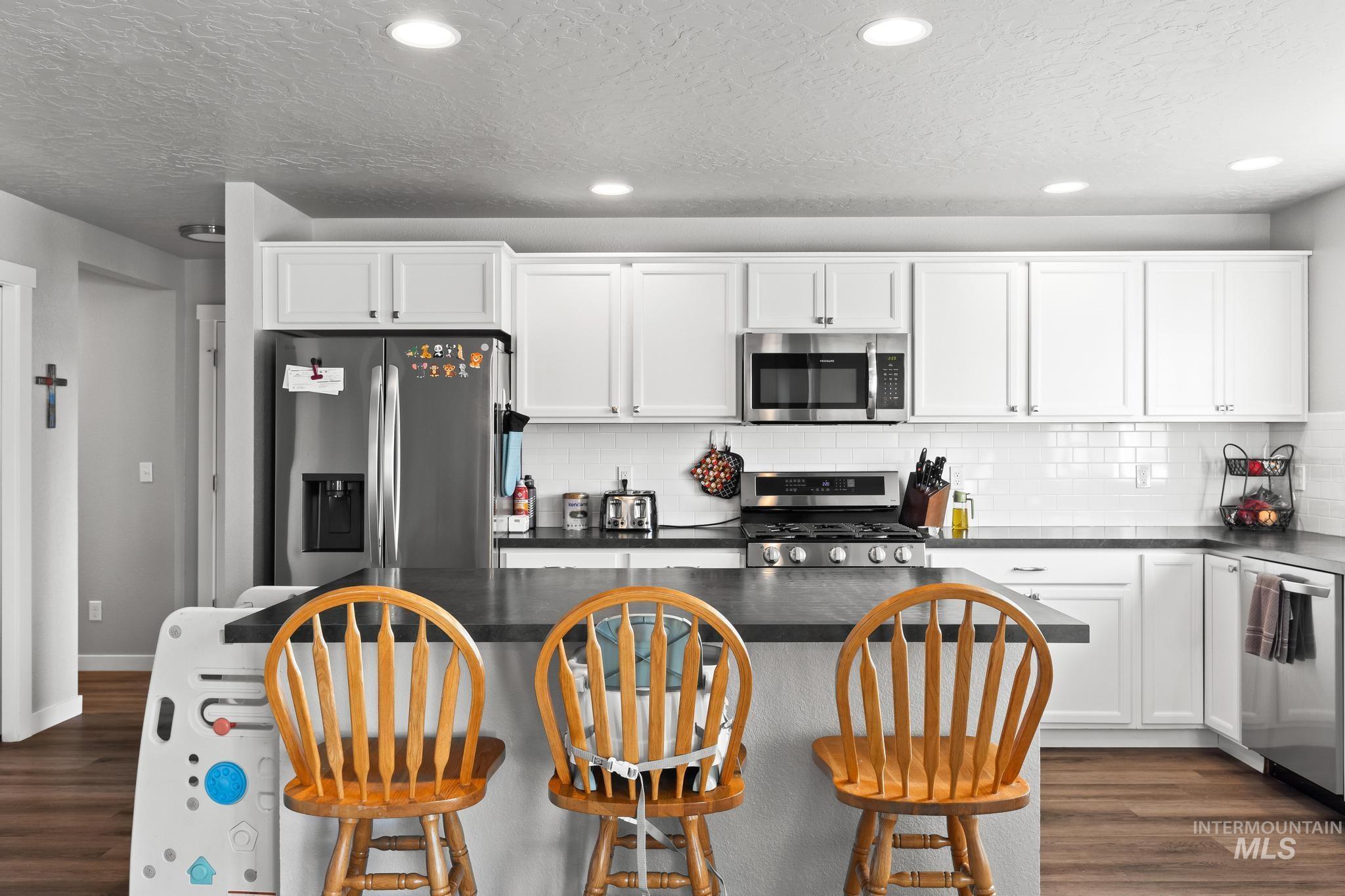 Kitchen featuring a breakfast bar, dark countertops, dark wood-type flooring, white cabinetry, and recessed lighting