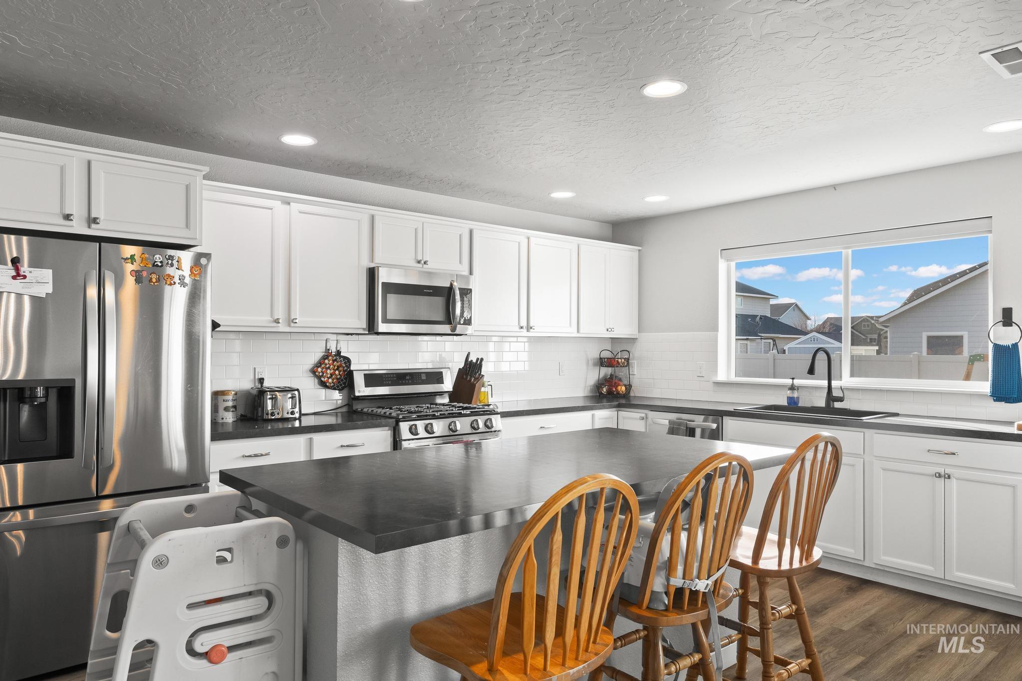 Kitchen with appliances with stainless steel finishes, recessed lighting, a kitchen bar, white cabinets, and dark wood-type flooring