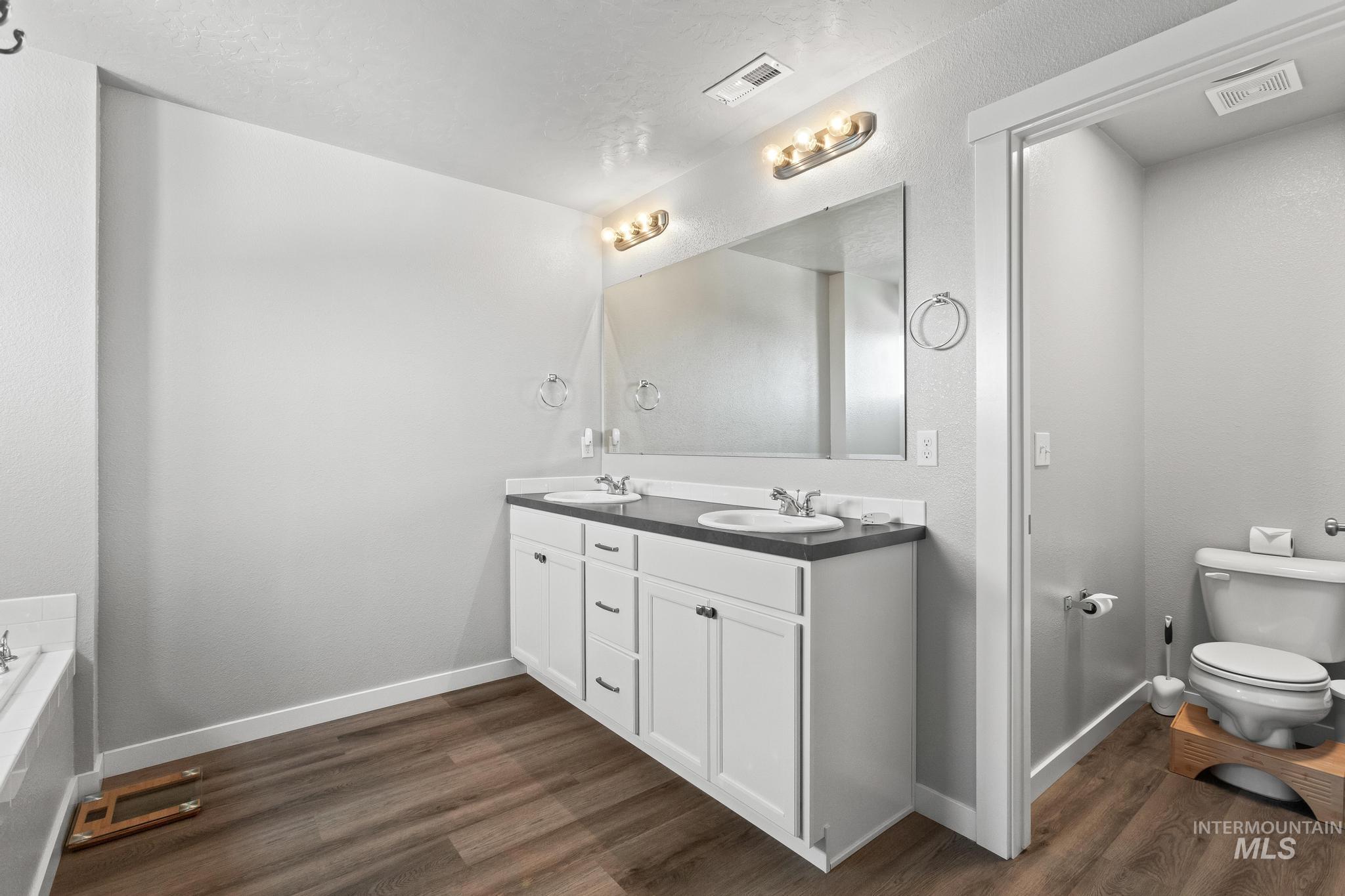 Full bathroom with double vanity, dark wood-style flooring, and a tub