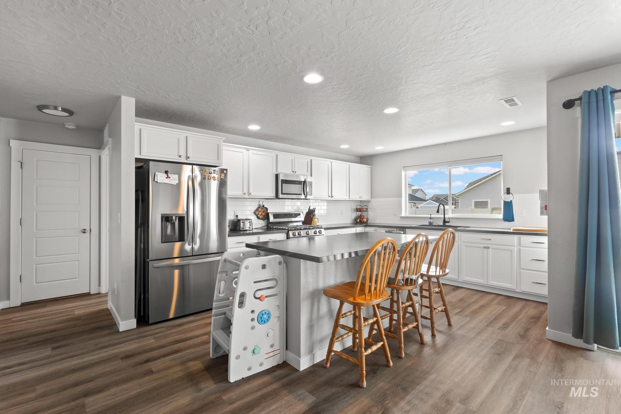 Kitchen with stainless steel appliances, white cabinetry, a breakfast bar area, a center island, and a textured ceiling