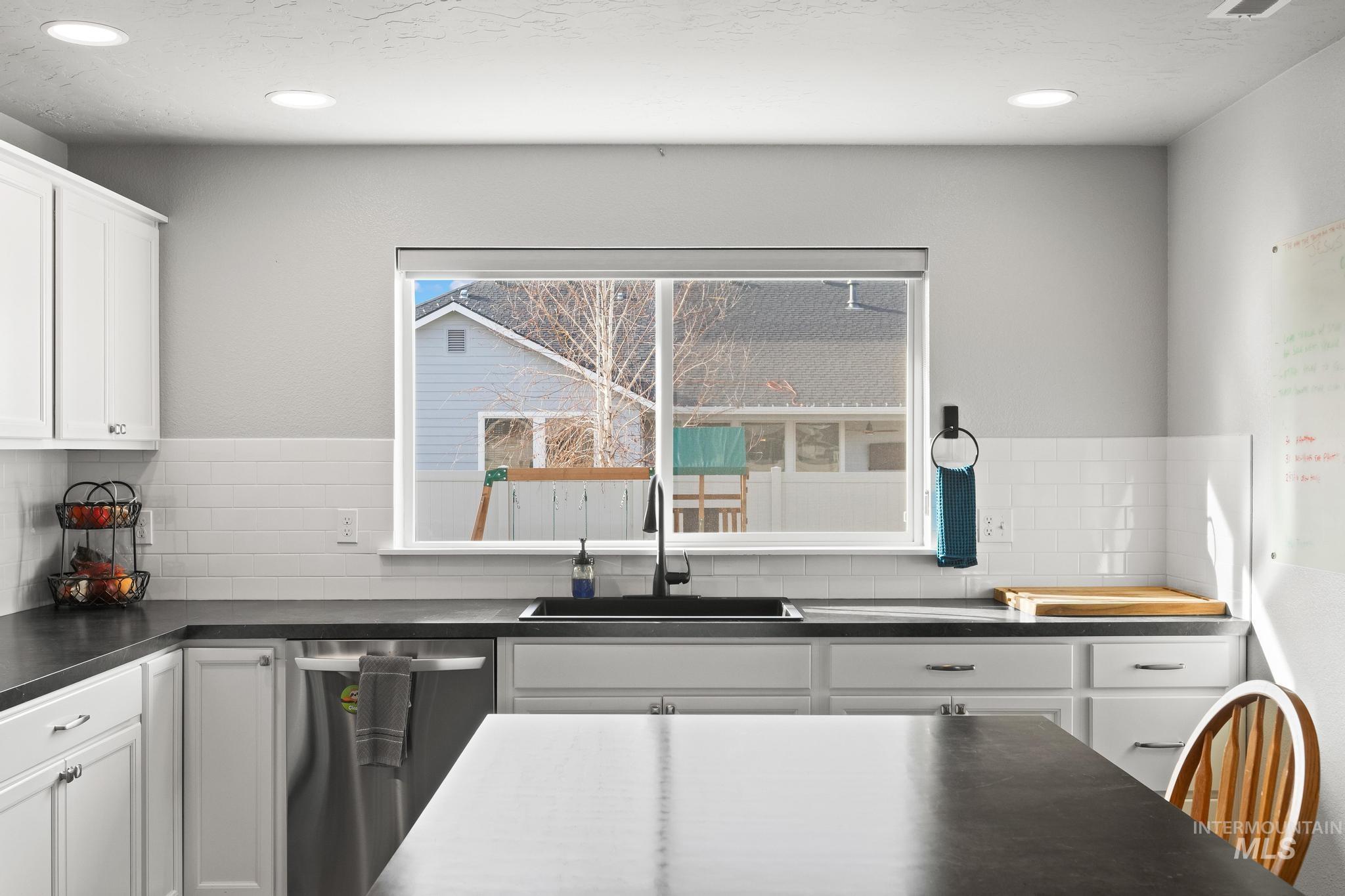 Kitchen with dark countertops, white cabinetry, backsplash, and recessed lighting