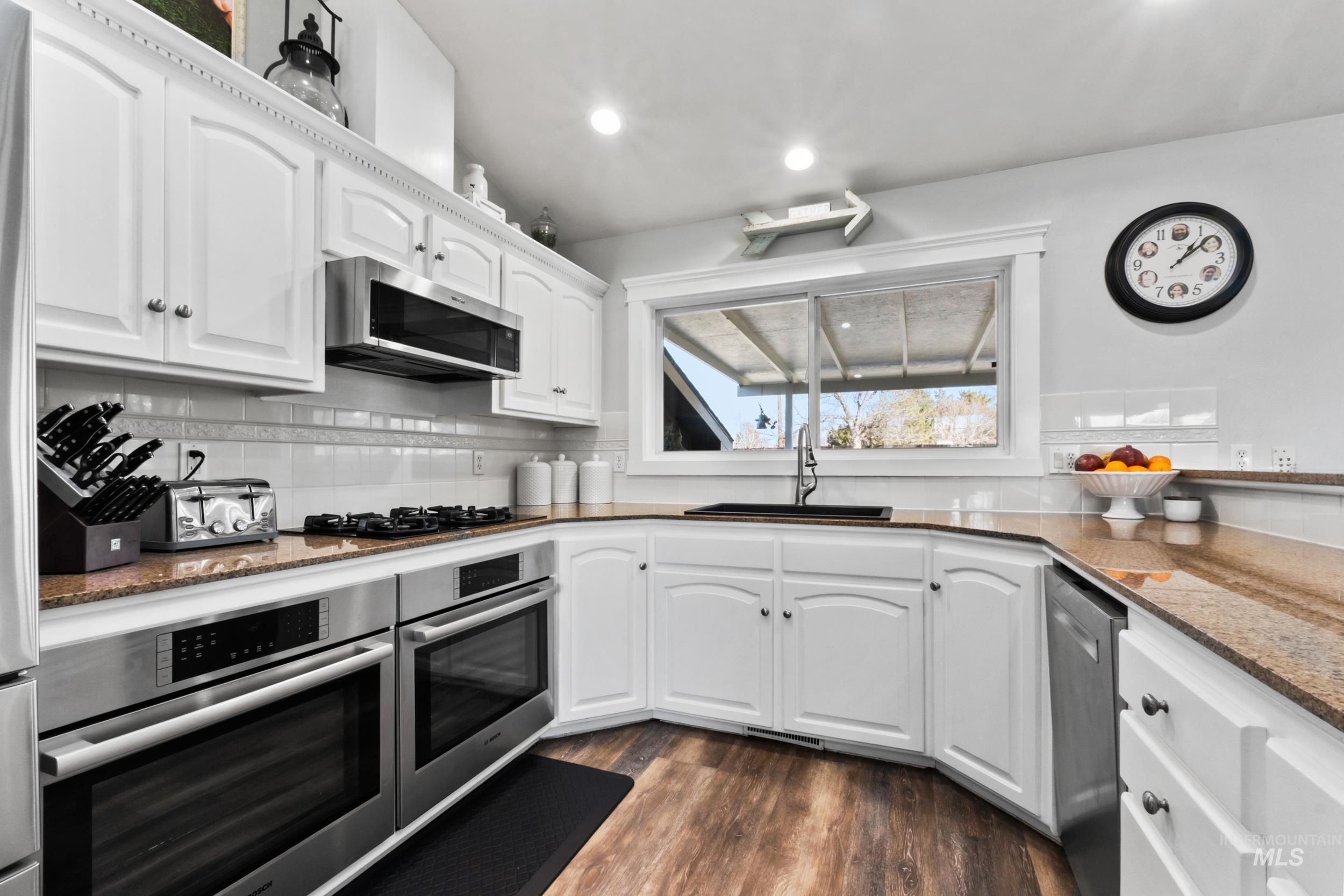Kitchen with white cabinetry, dark stone countertops, appliances with stainless steel finishes, dark wood-type flooring, and recessed lighting