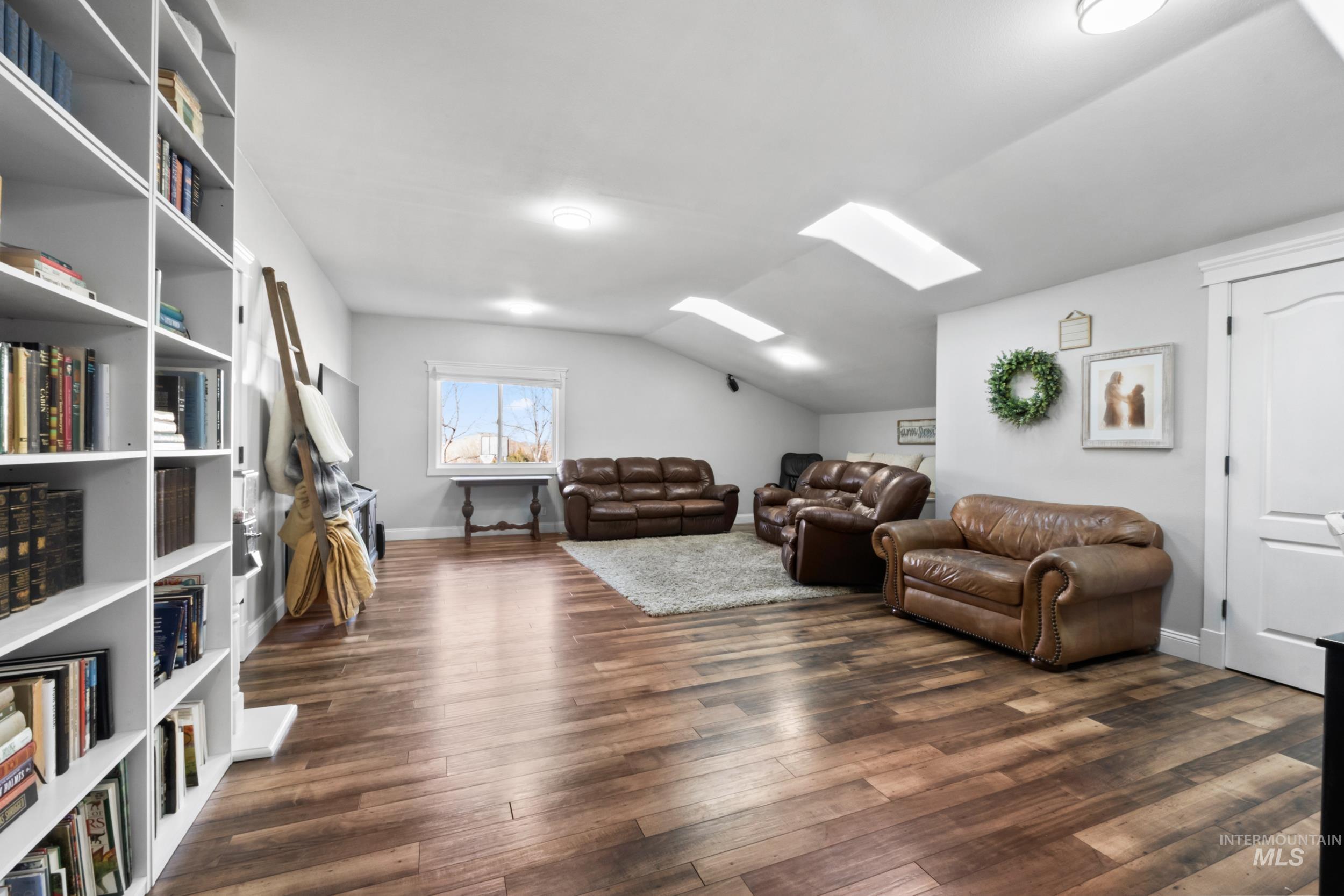 Living room with a skylight, dark wood-style flooring, and lofted ceiling