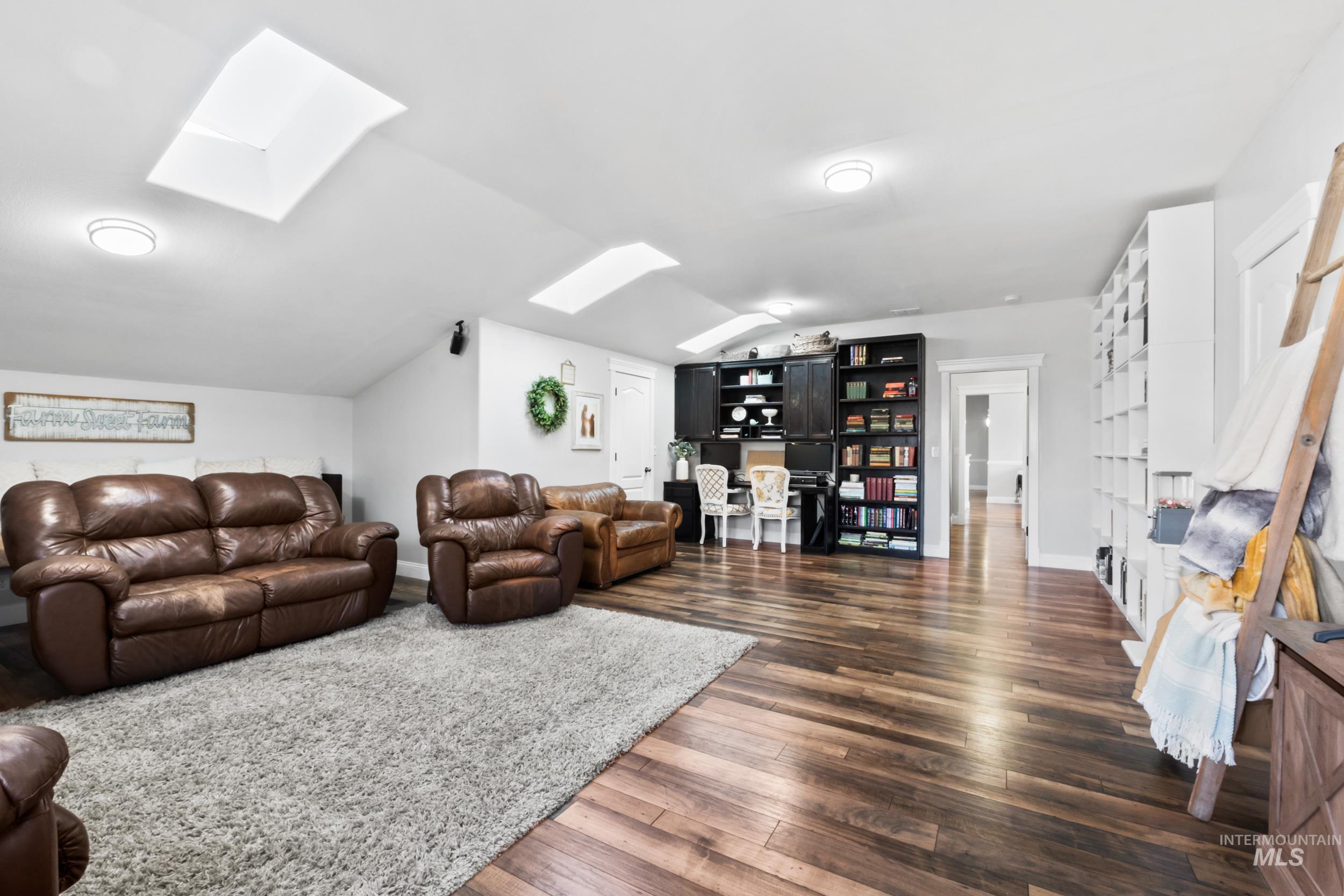 Living room featuring a skylight, vaulted ceiling, and dark wood-style flooring