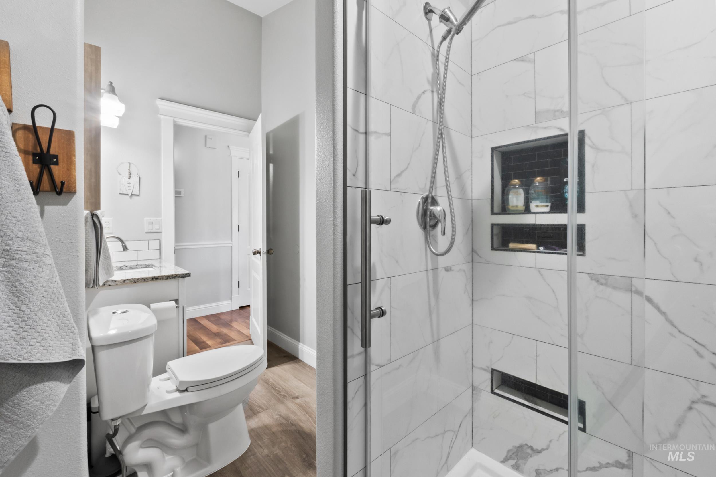 Bathroom featuring vanity, a marble finish shower, and dark wood-type flooring