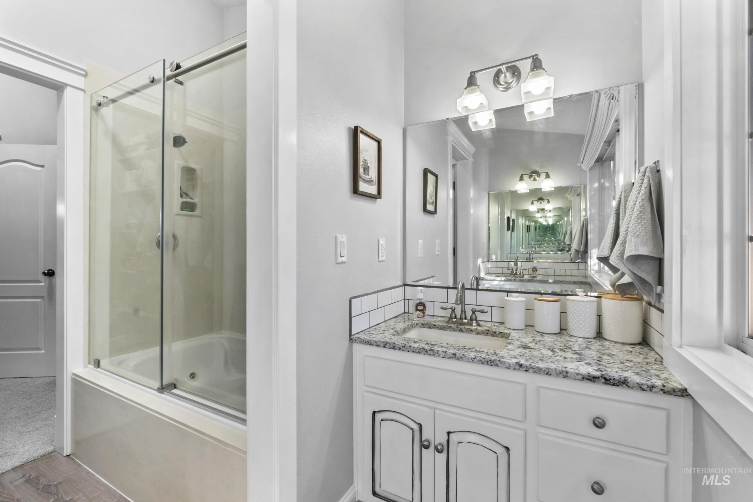 Bathroom with vanity, enclosed tub / shower combo, and wood finished floors