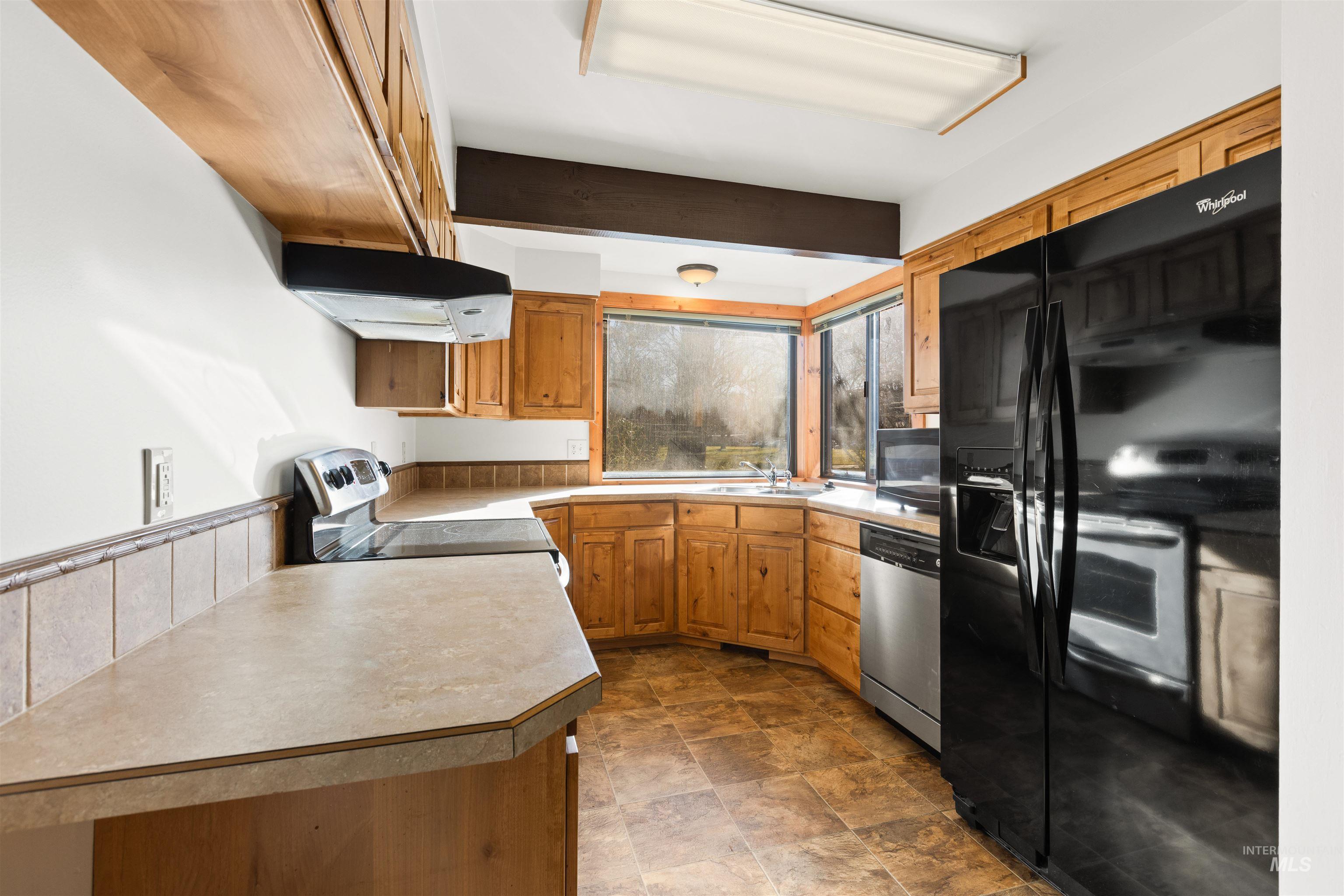 Kitchen featuring black appliances, light countertops, under cabinet range hood, stone finish floors, and brown cabinets
