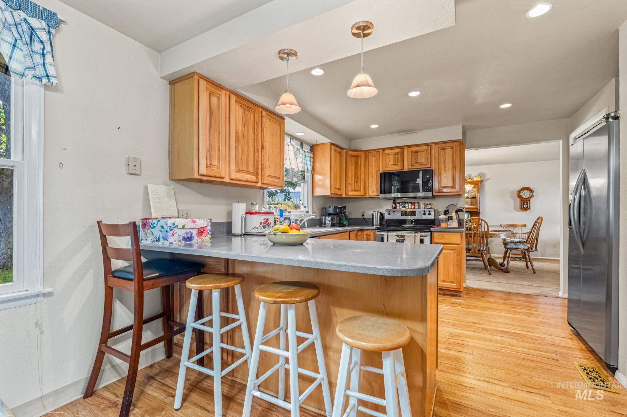 Kitchen with a peninsula, pendant lighting, stainless steel appliances, light wood-type flooring, and a kitchen bar