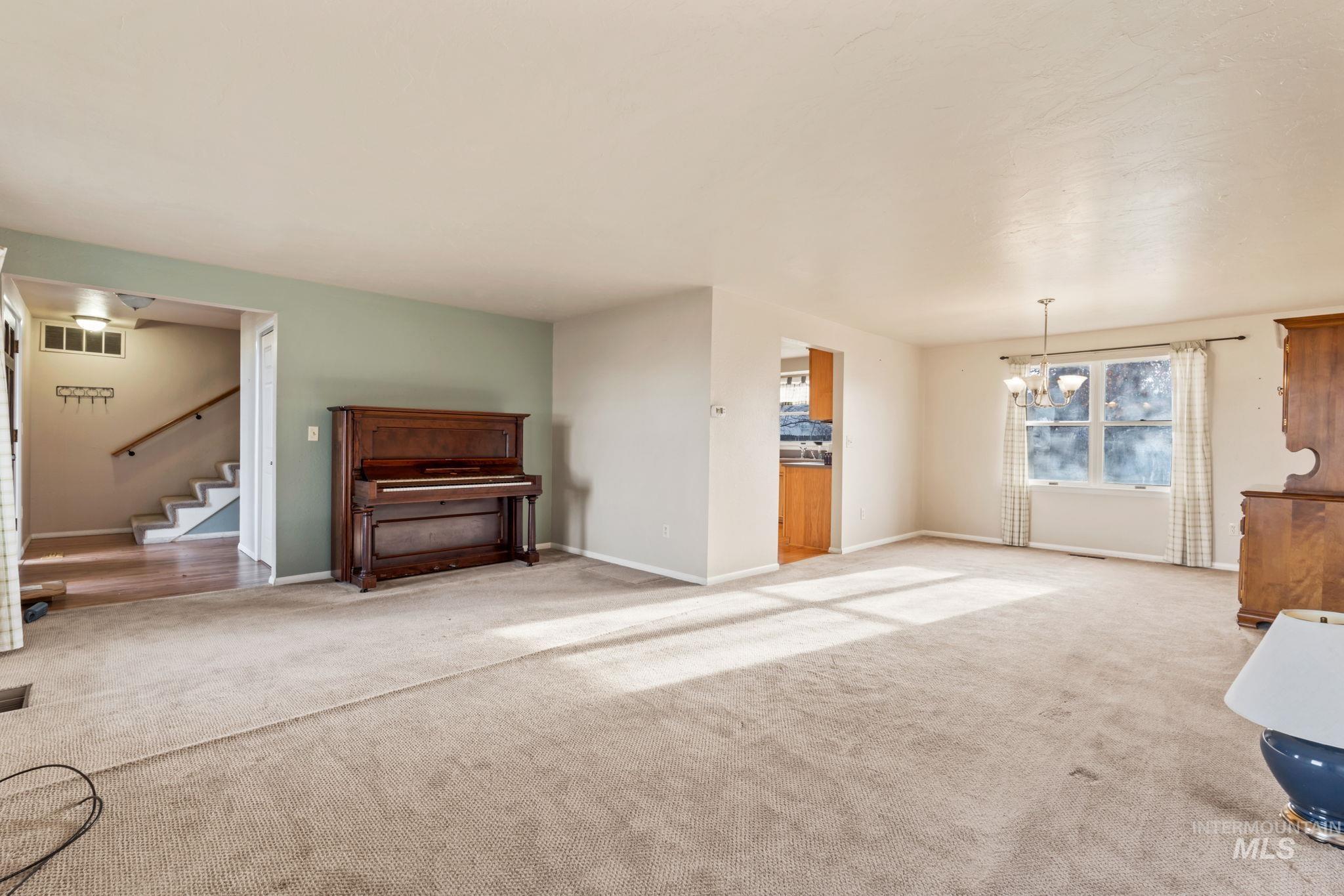 Unfurnished living room featuring carpet floors, a chandelier, and stairs