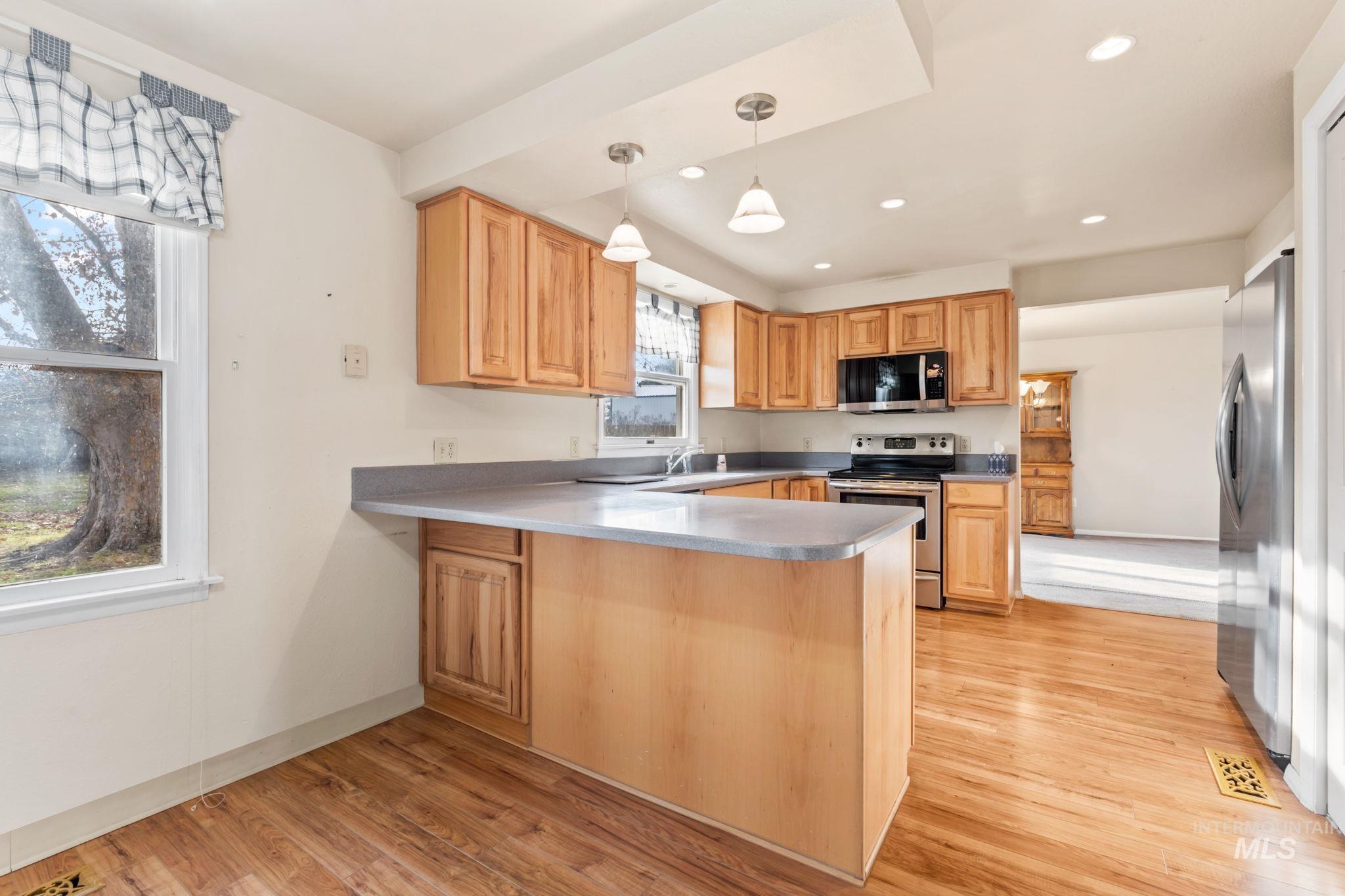 Kitchen with a peninsula, hanging light fixtures, stainless steel appliances, light wood-style floors, and light brown cabinets