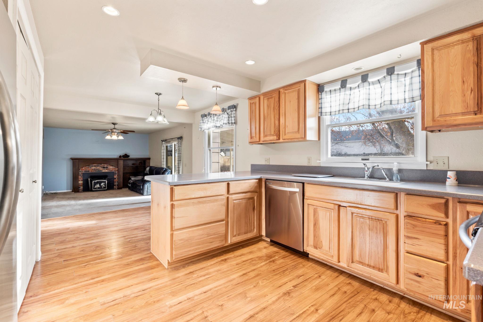 Kitchen with a brick fireplace, a peninsula, stainless steel appliances, a ceiling fan, and light brown cabinets