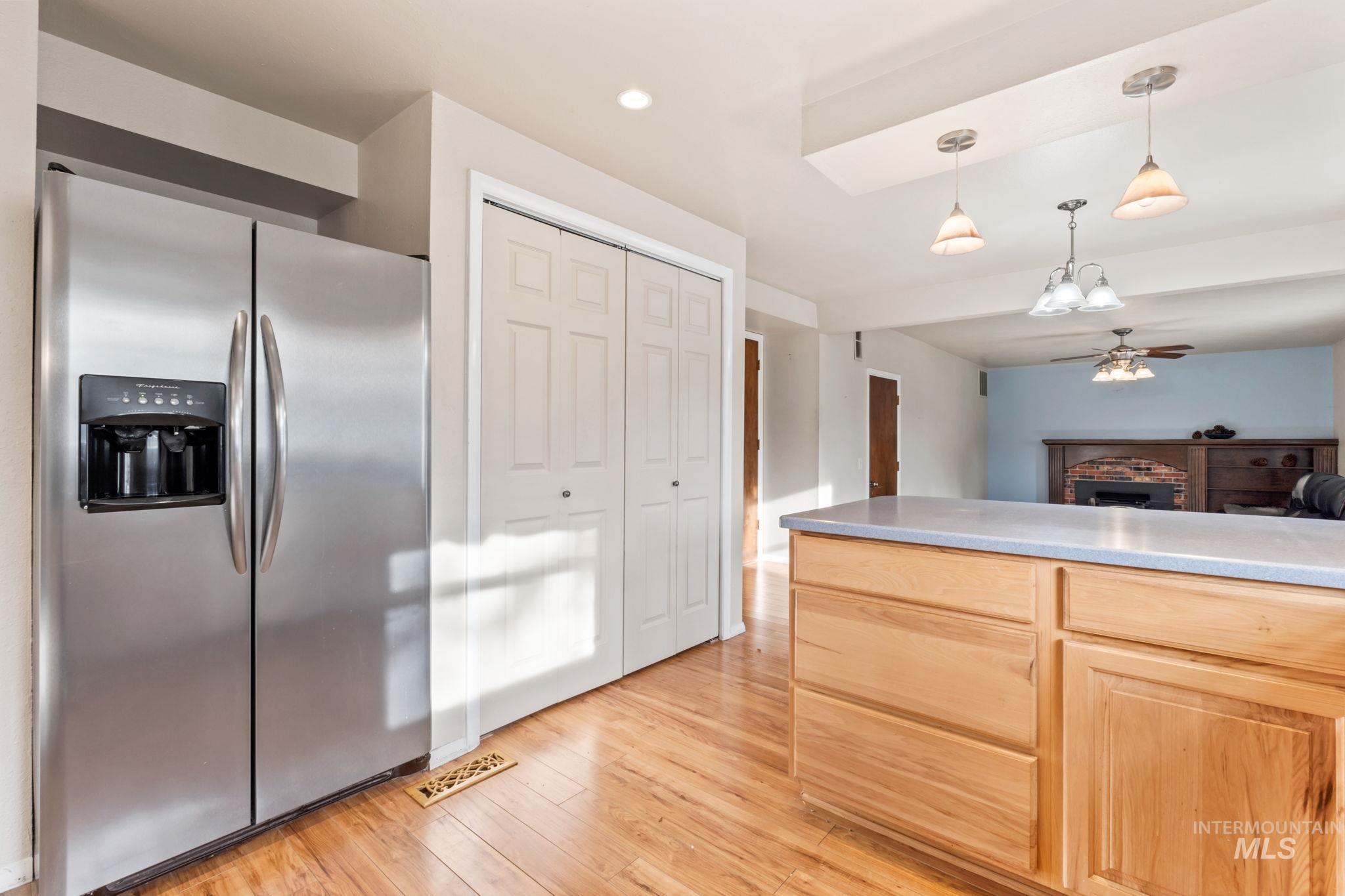 Kitchen with stainless steel refrigerator with ice dispenser, a fireplace, light brown cabinetry, light countertops, and light wood finished floors