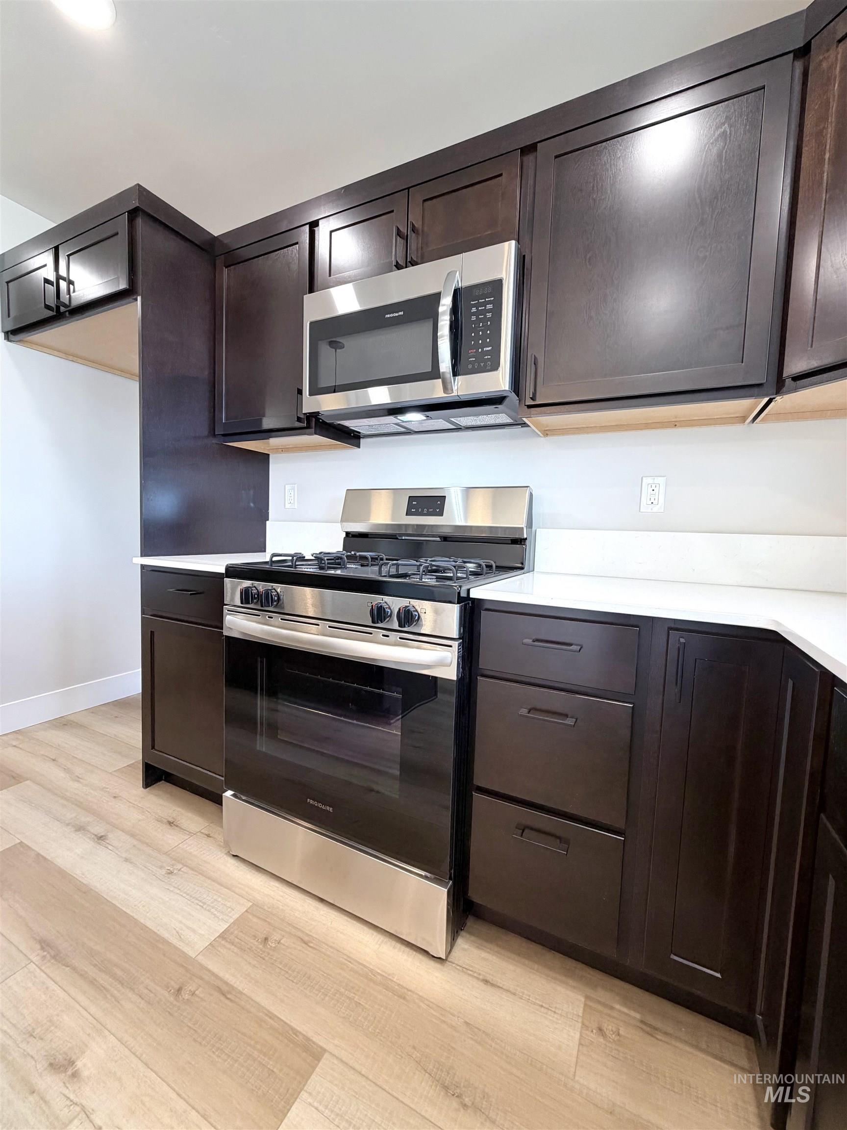 Kitchen with stainless steel appliances, dark brown cabinetry, and light wood finished floors