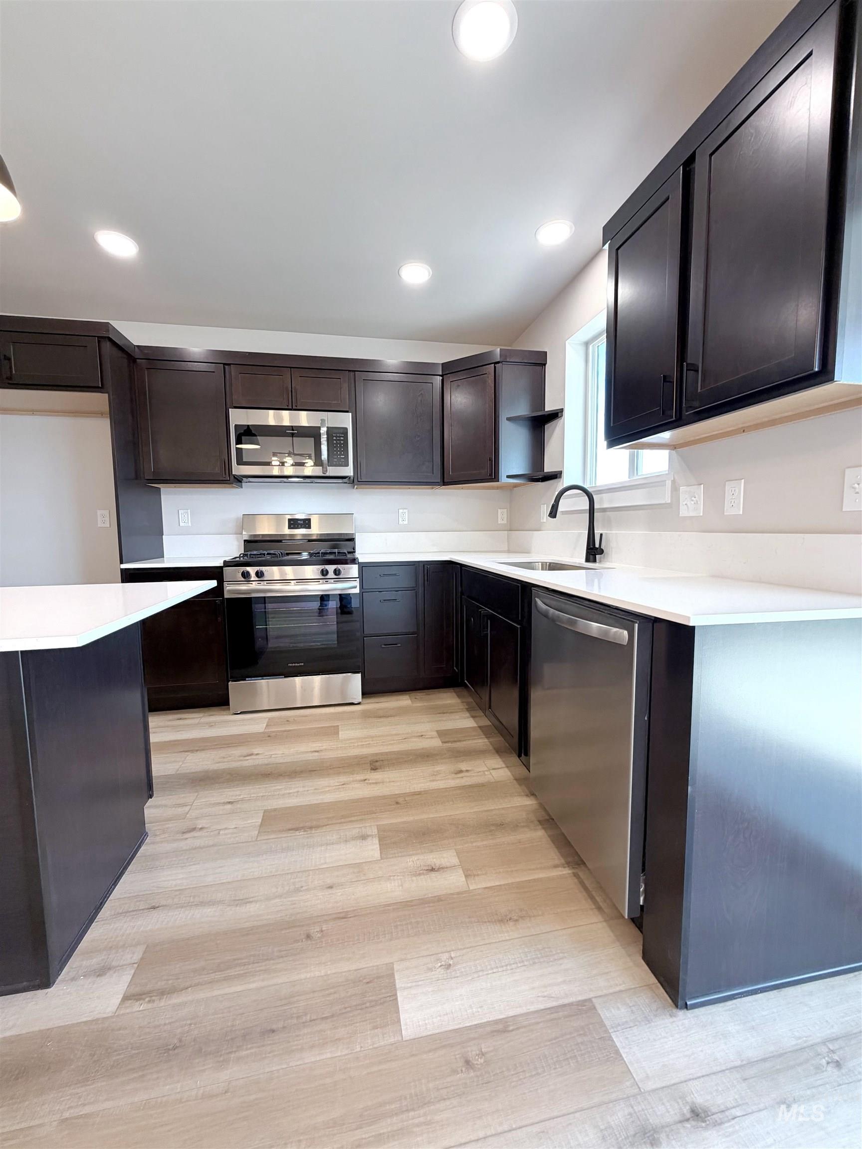 Kitchen featuring appliances with stainless steel finishes, light wood-type flooring, open shelves, recessed lighting, and dark brown cabinetry